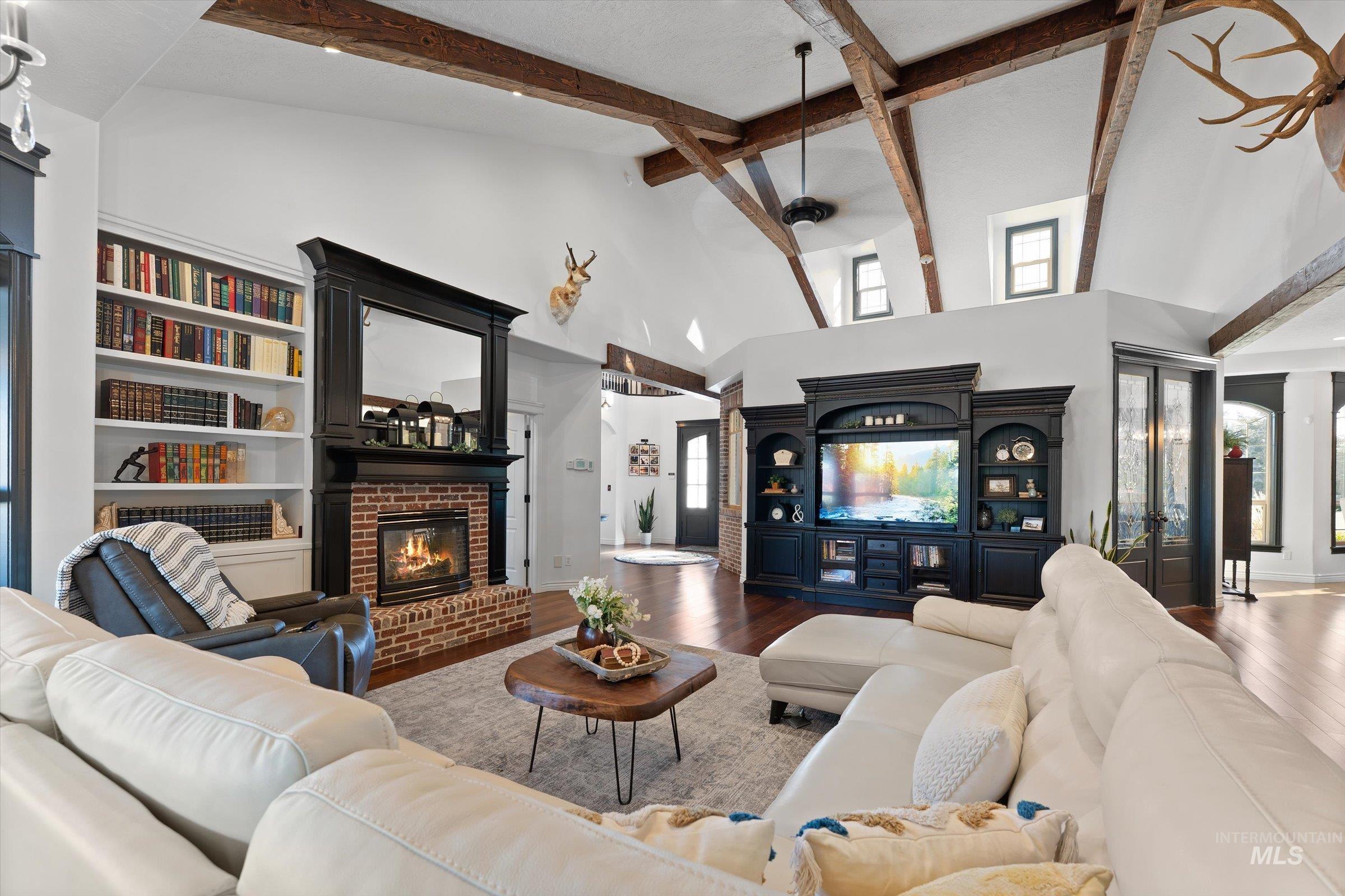 Living room with high vaulted ceiling, a fireplace, wood finished floors, beam ceiling, and a ceiling fan