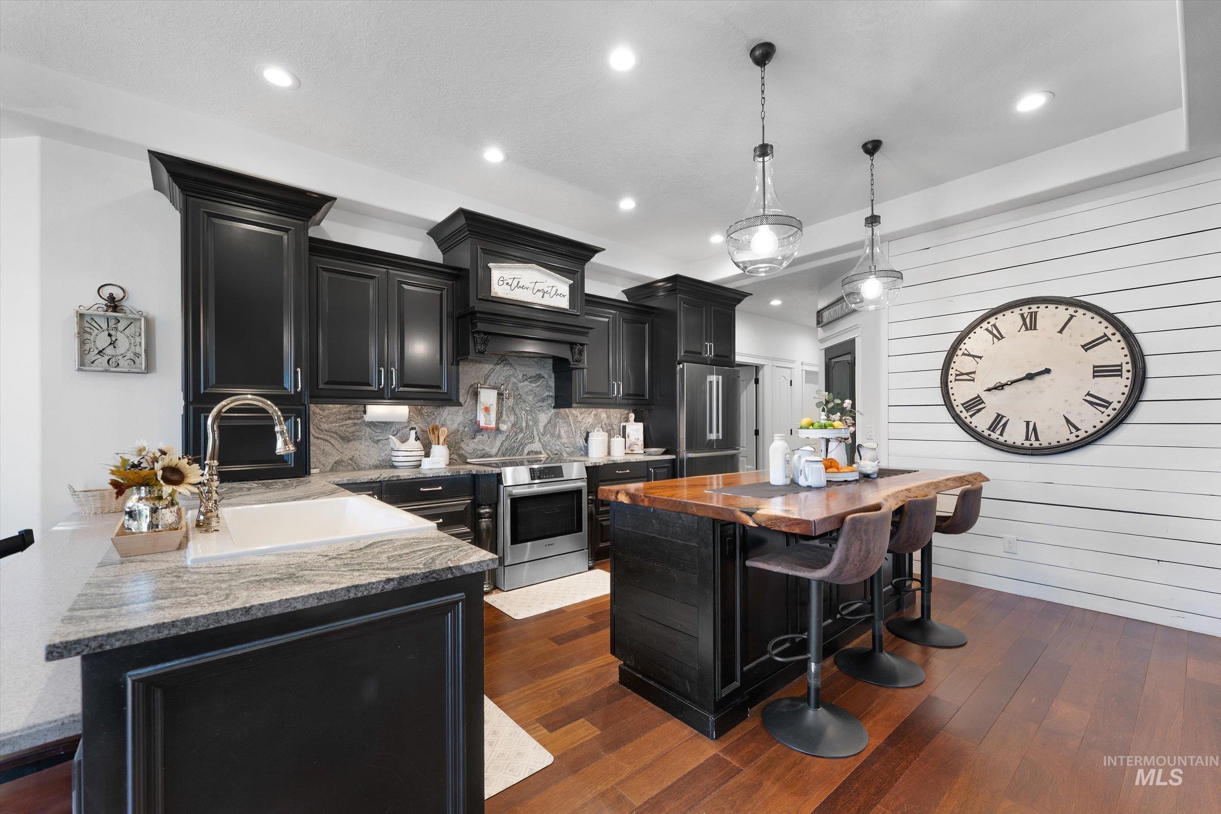 Kitchen with dark cabinets, a breakfast bar area, dark stone counters, dark wood-style flooring, and hanging light fixtures