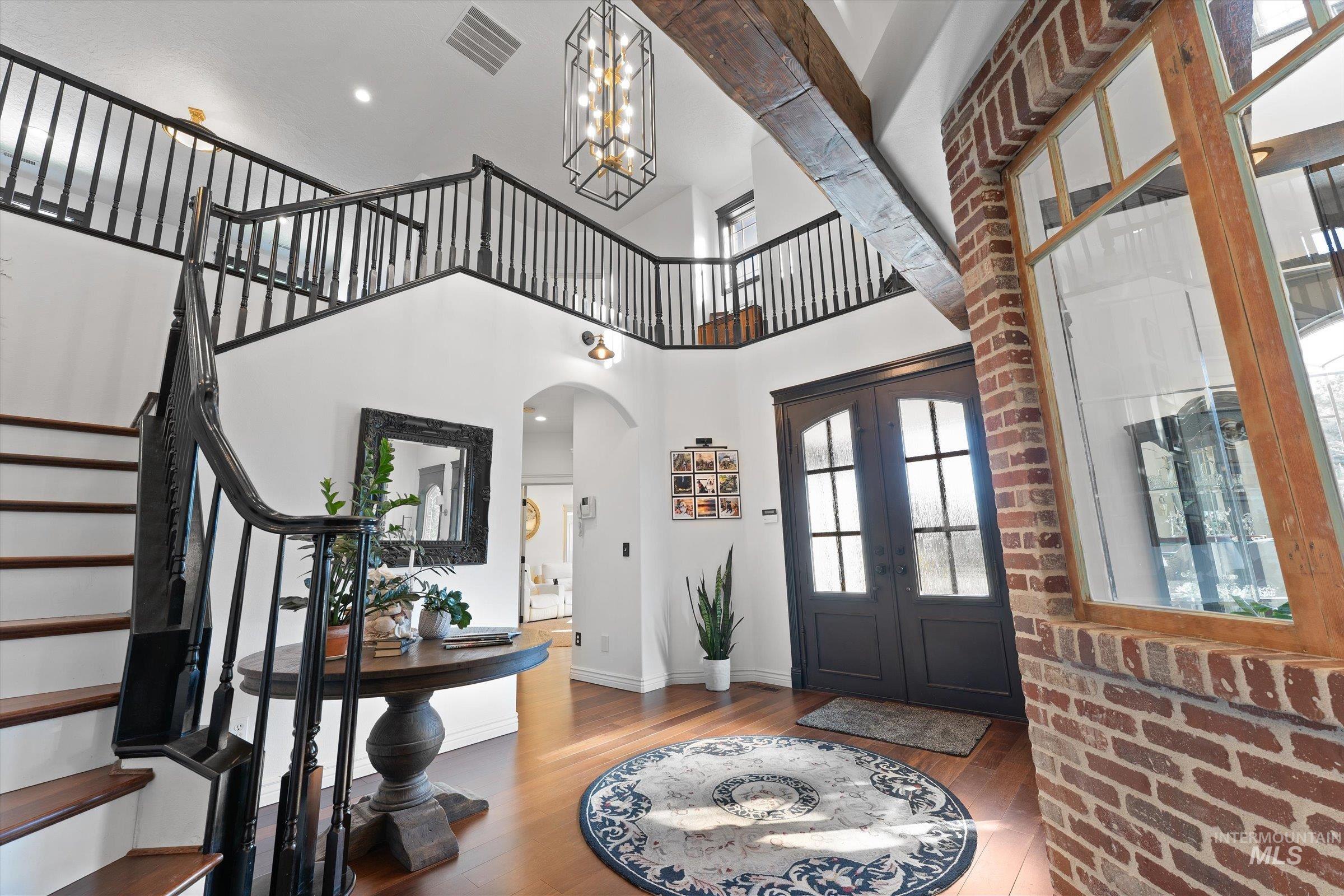 Entrance foyer featuring wood finished floors, arched walkways, french doors, a towering ceiling, and a chandelier