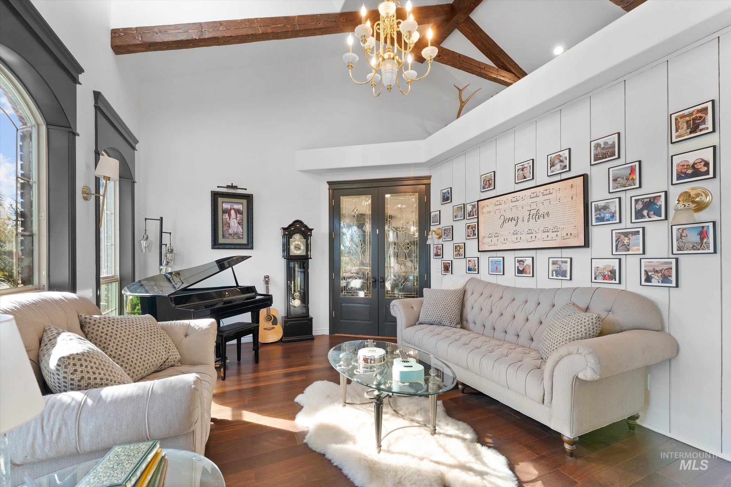 Living room with high vaulted ceiling, healthy amount of natural light, a chandelier, wood finished floors, and beamed ceiling