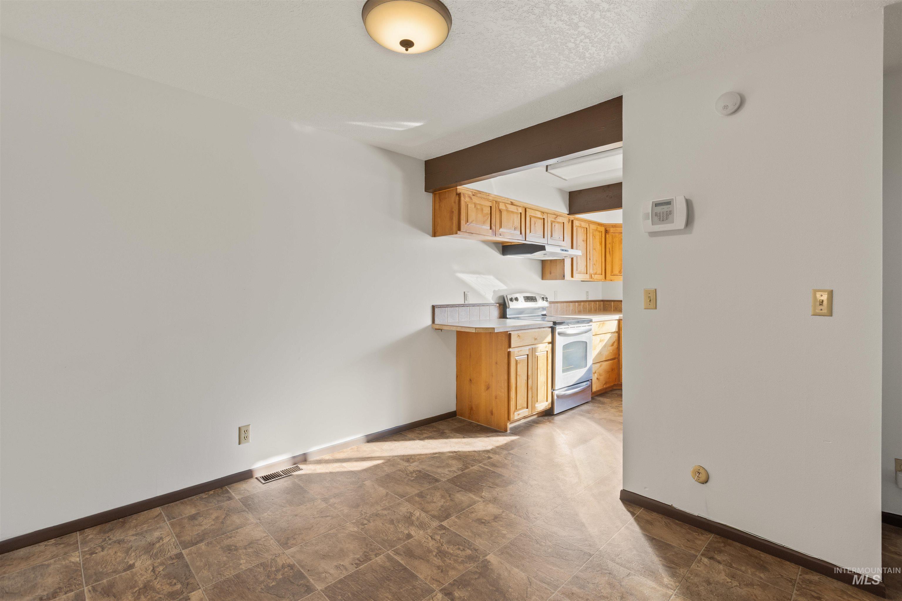 Kitchen with light countertops, stainless steel electric stove, a textured ceiling, and under cabinet range hood