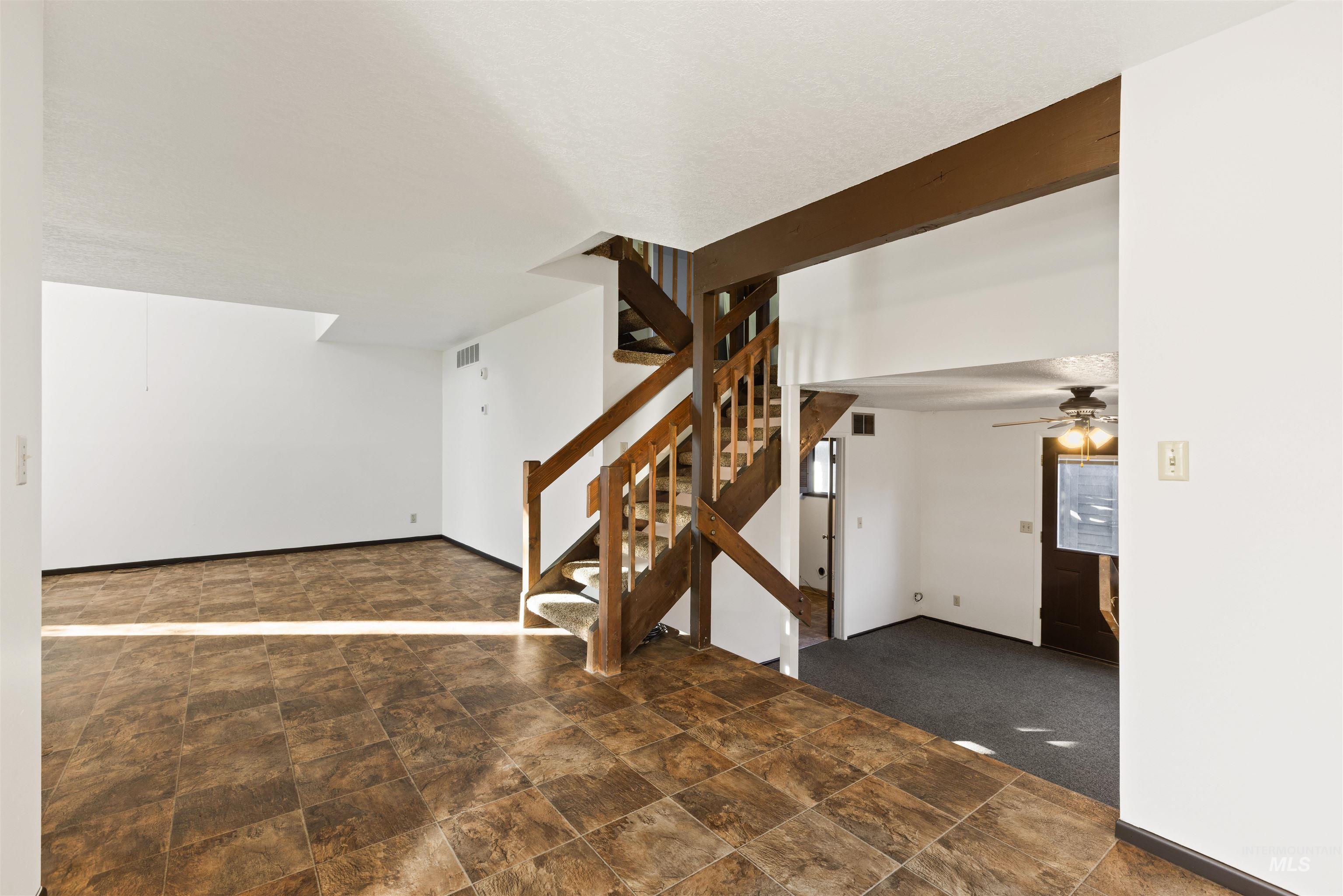Unfurnished living room featuring stone finish floors, stairway, a ceiling fan, and dark colored carpet