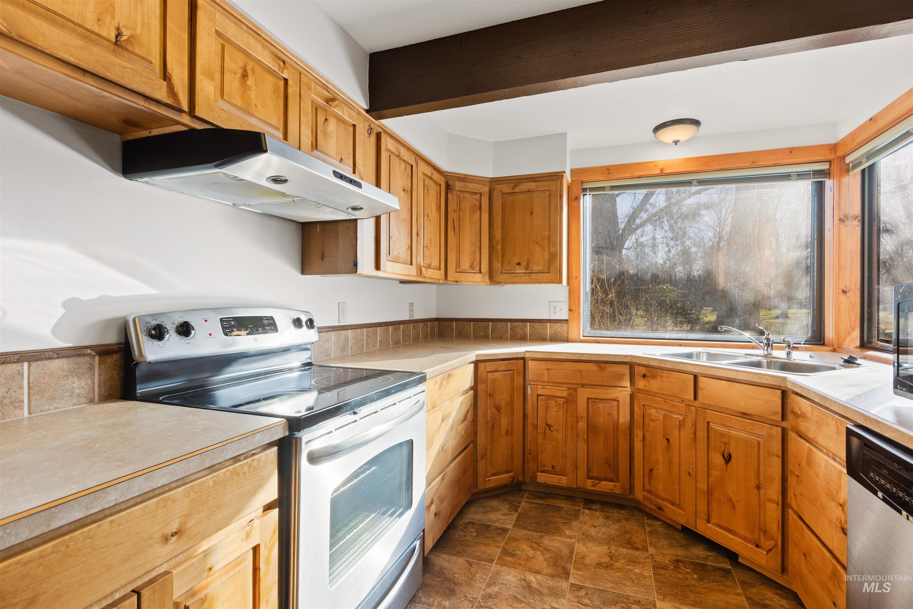 Kitchen featuring appliances with stainless steel finishes, under cabinet range hood, light countertops, brown cabinets, and stone finish floors