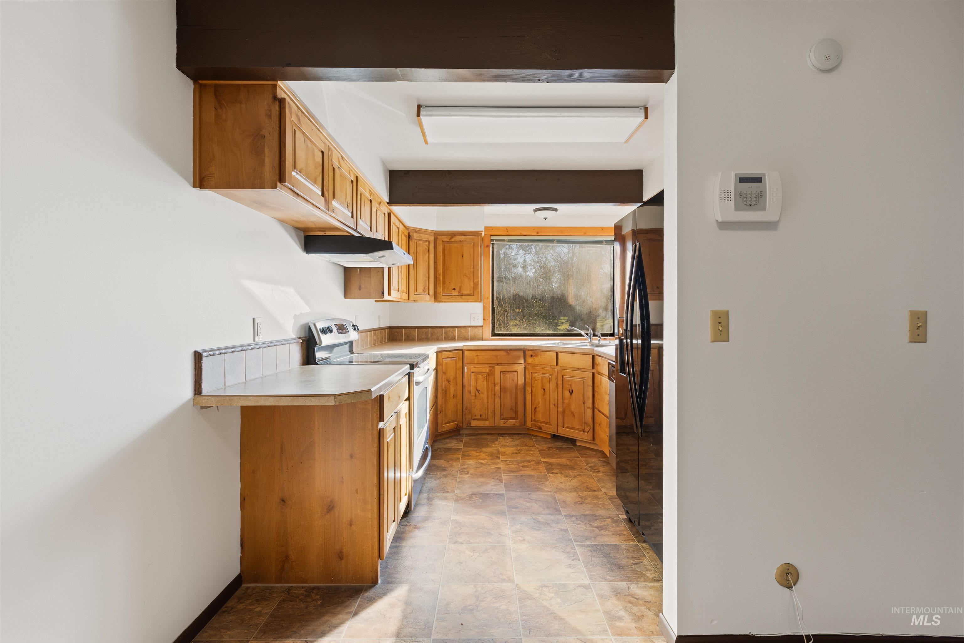 Kitchen featuring stainless steel electric stove, light countertops, refrigerator with ice dispenser, brown cabinets, and under cabinet range hood