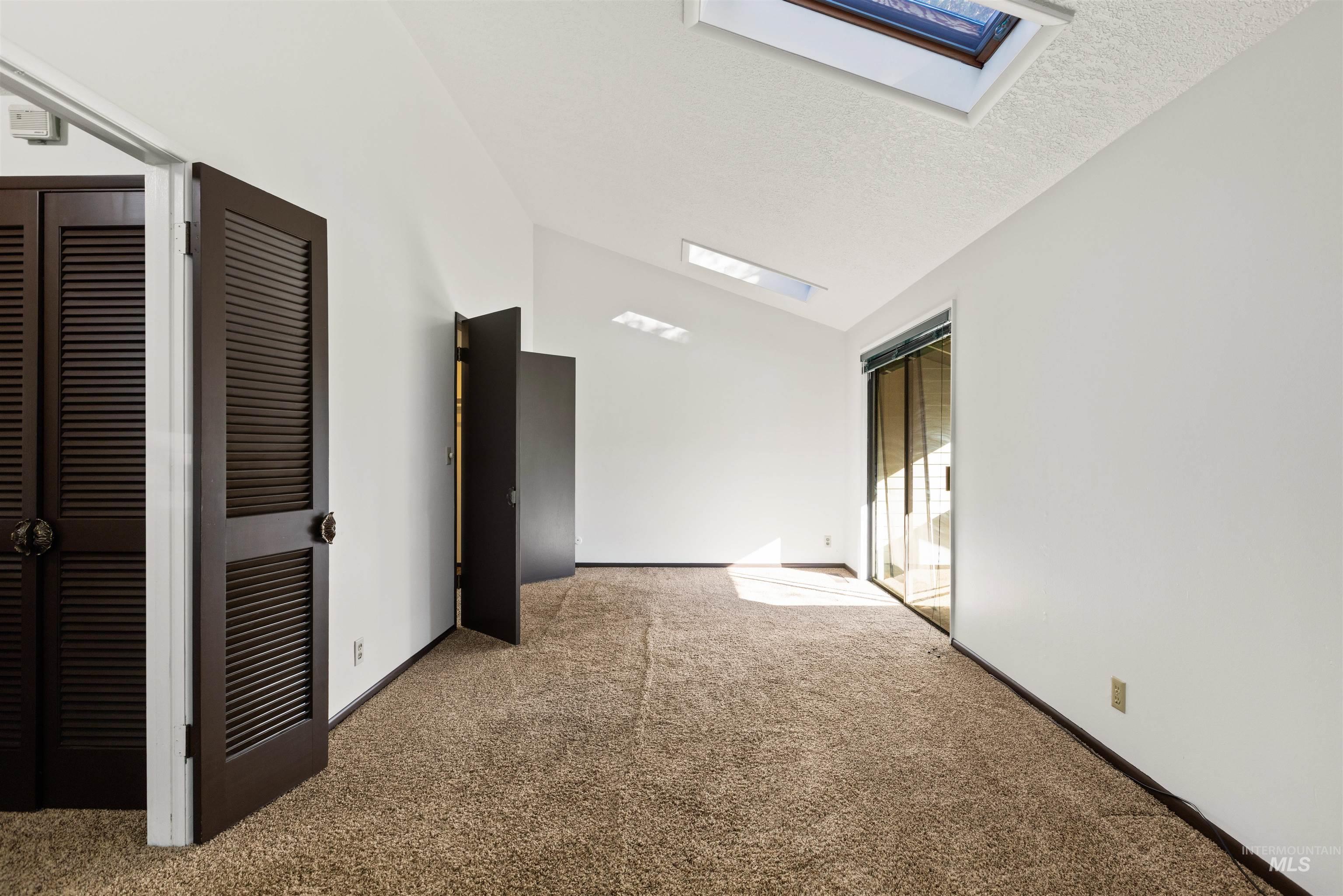 Unfurnished room featuring carpet flooring, a skylight, a textured ceiling, and high vaulted ceiling