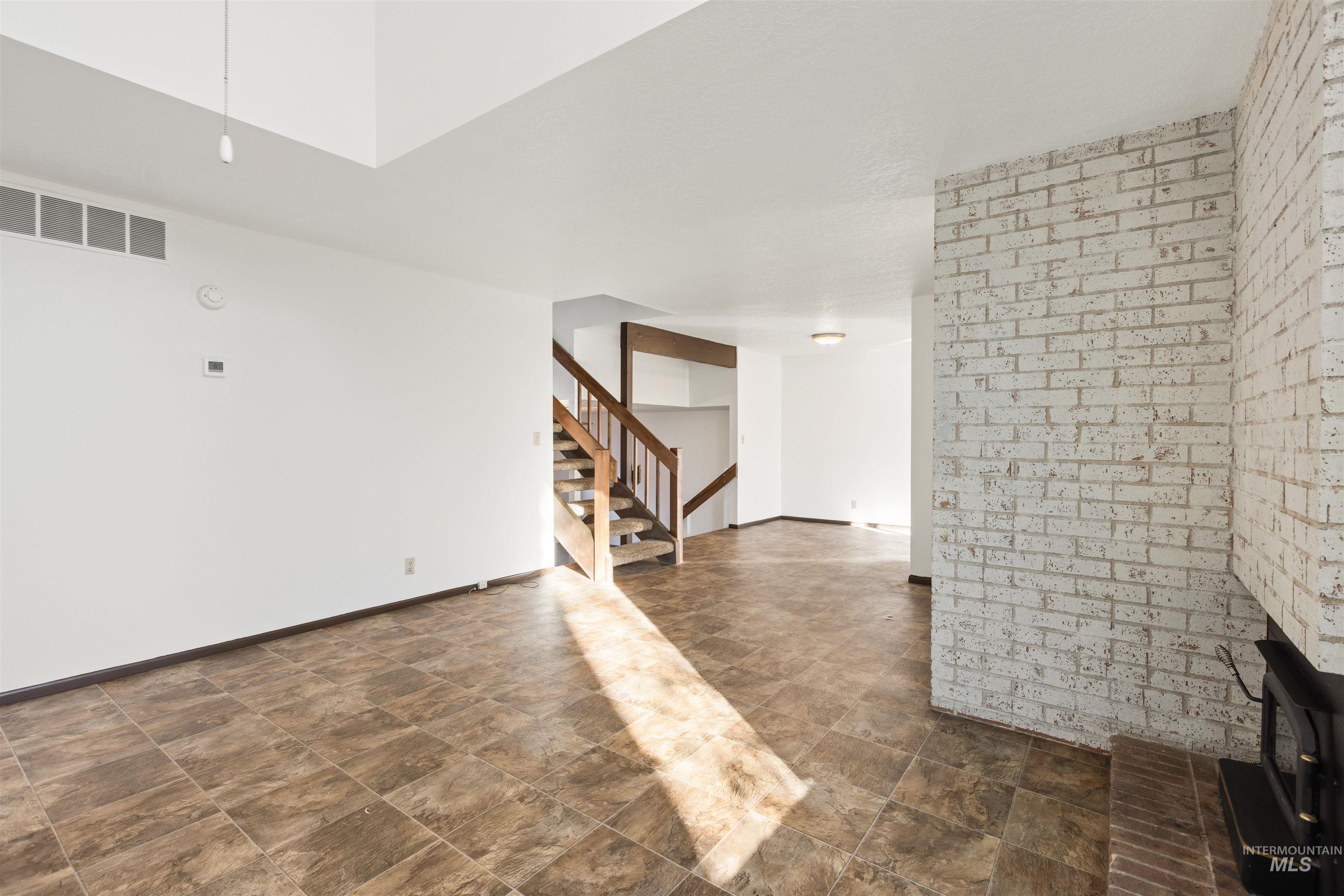 Unfurnished living room with stone finish flooring, brick wall, and stairs
