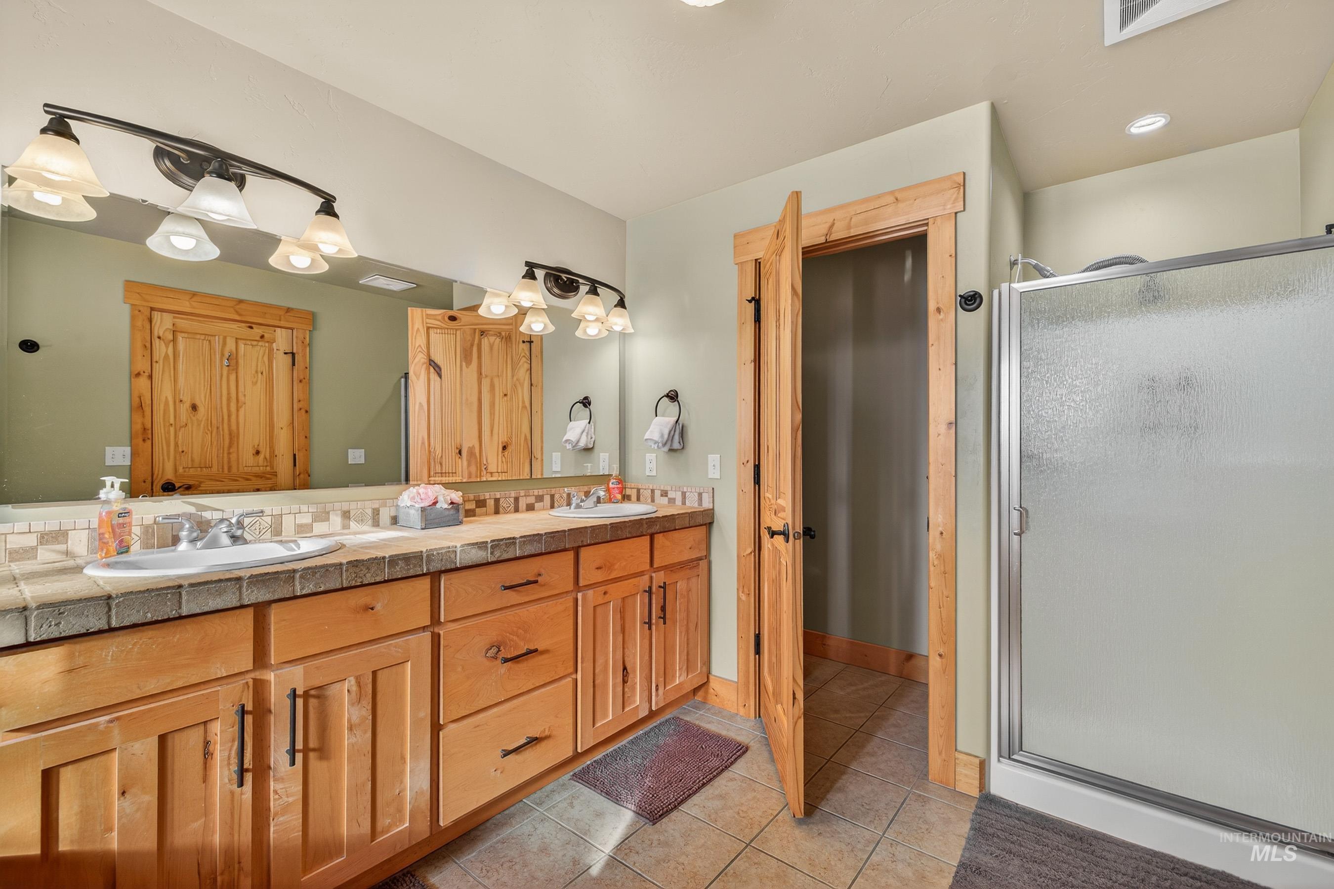 Full bathroom featuring double vanity, light tile patterned floors, and a shower stall