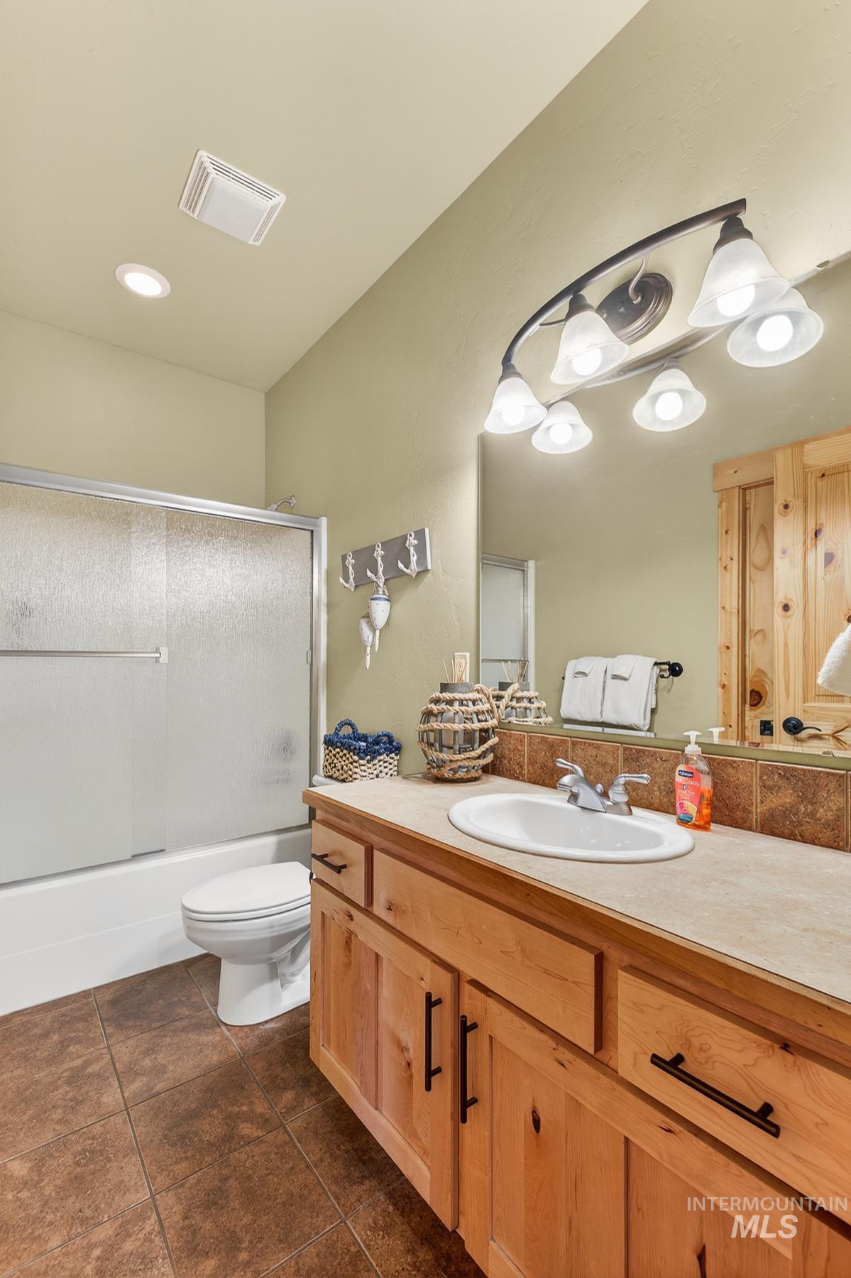Bathroom featuring vanity, enclosed tub / shower combo, and dark tile patterned flooring