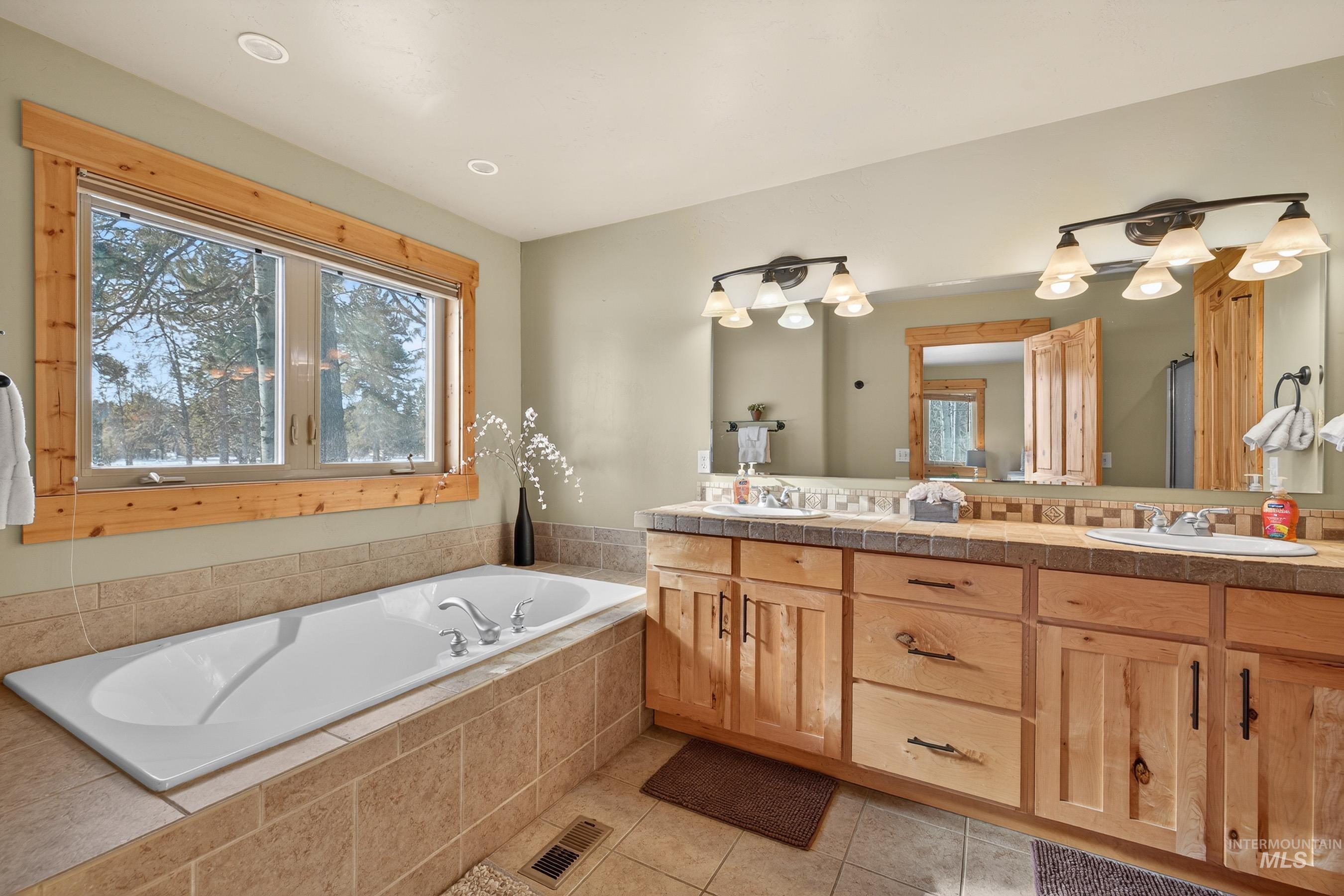 Full bath featuring double vanity, a garden tub, and light tile patterned flooring
