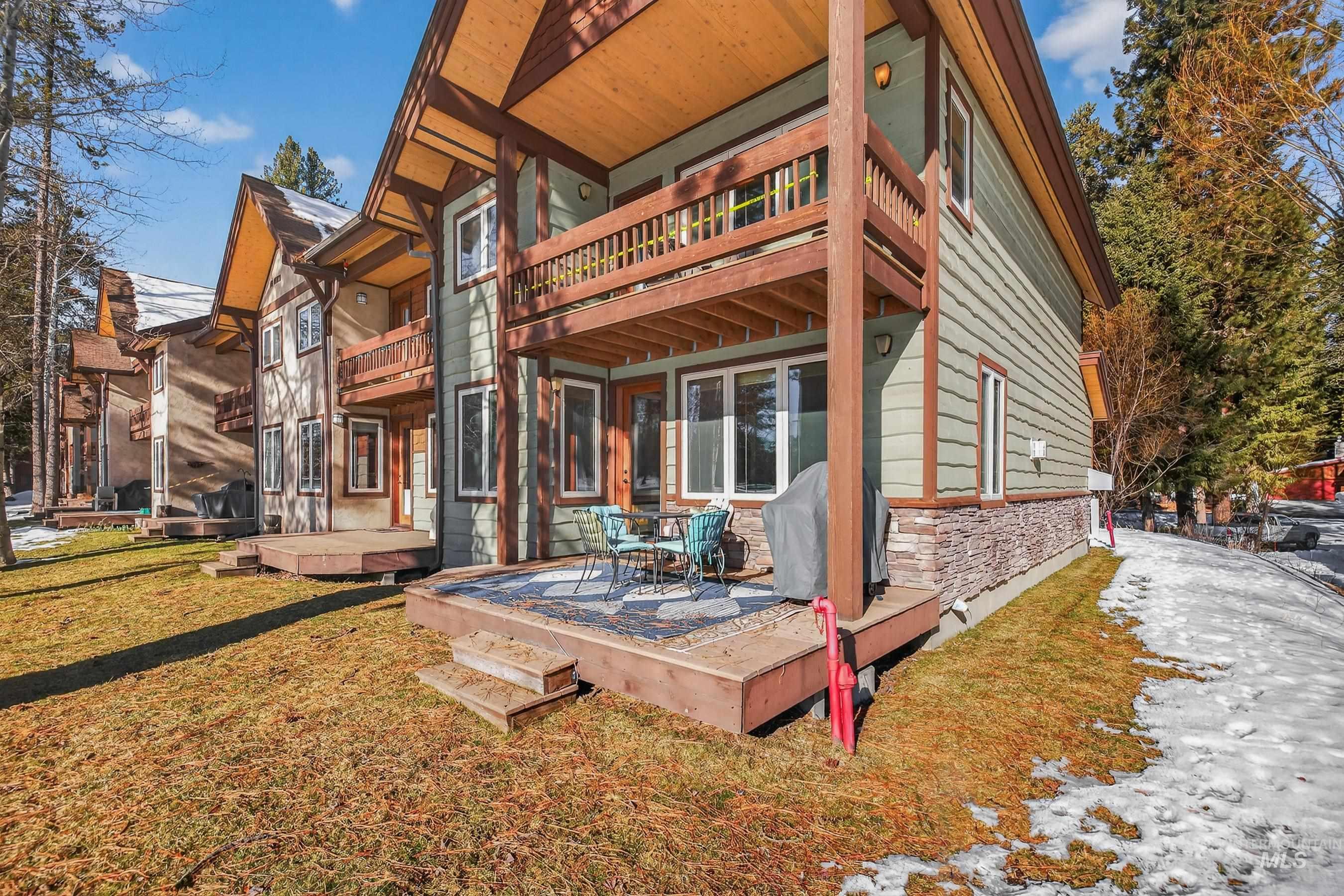 Back of house featuring a balcony, stone siding, a wooden deck, and a yard