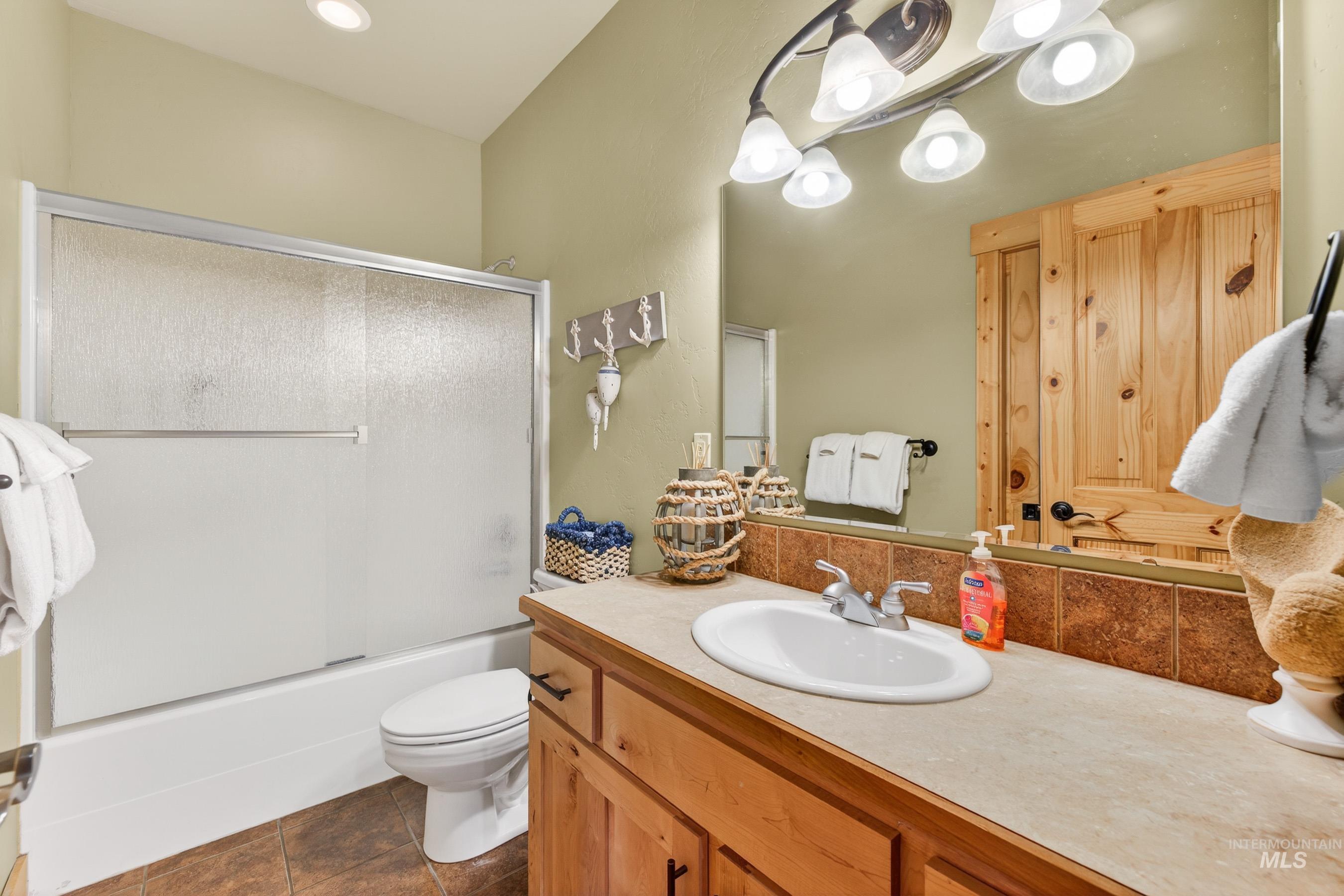 Bathroom with vanity, enclosed tub / shower combo, and dark tile patterned flooring