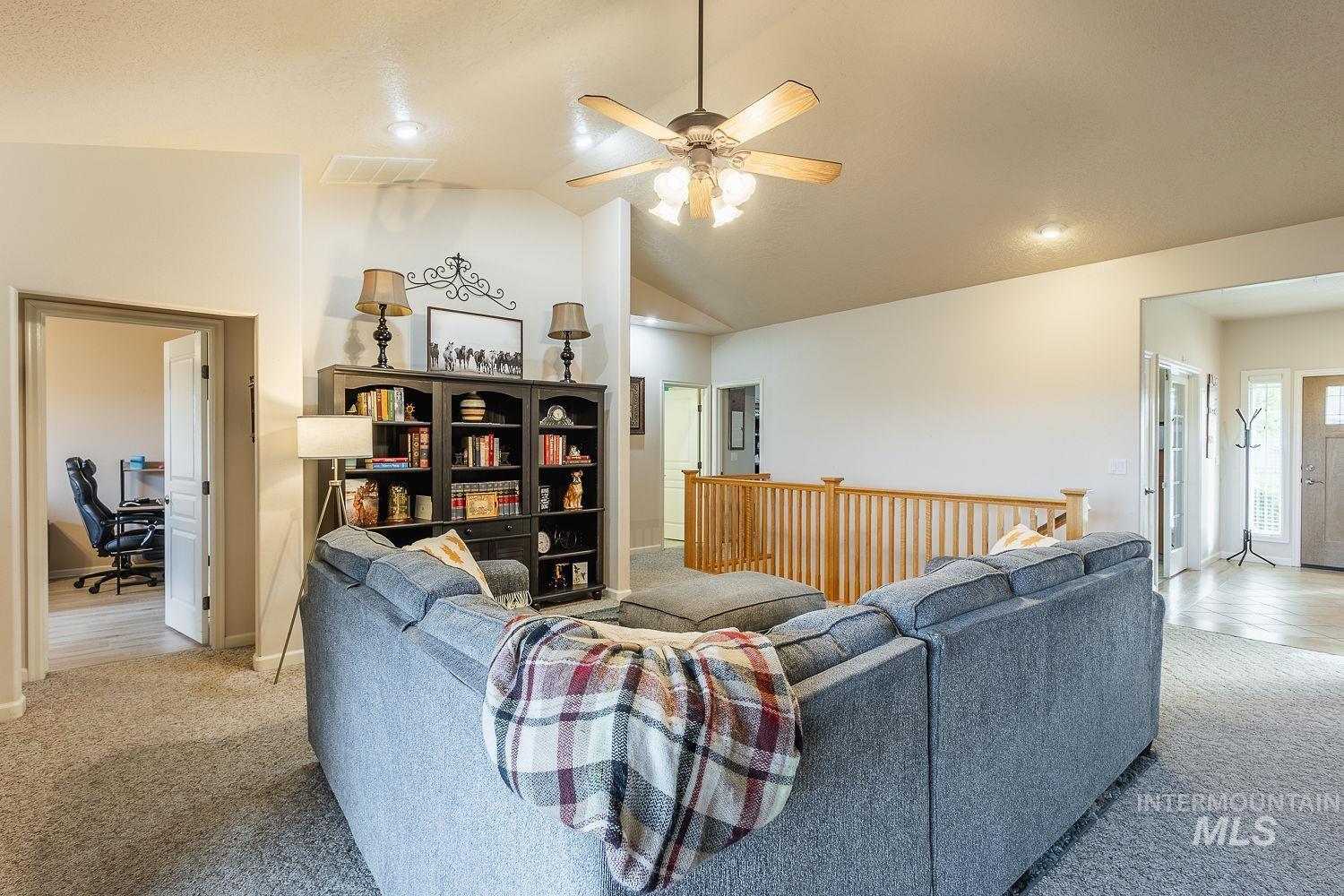 Carpeted living room featuring a desk, vaulted ceiling, and ceiling fan