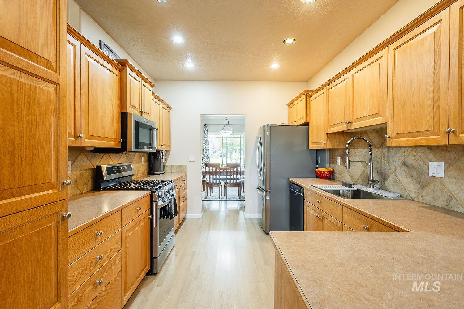 Kitchen with stainless steel appliances, tasteful backsplash, light wood-style flooring, light countertops, and recessed lighting