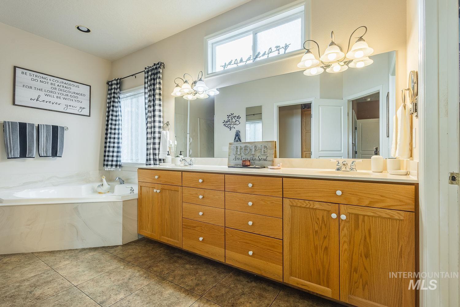 Full bath with plenty of natural light, double vanity, a garden tub, and dark tile patterned flooring
