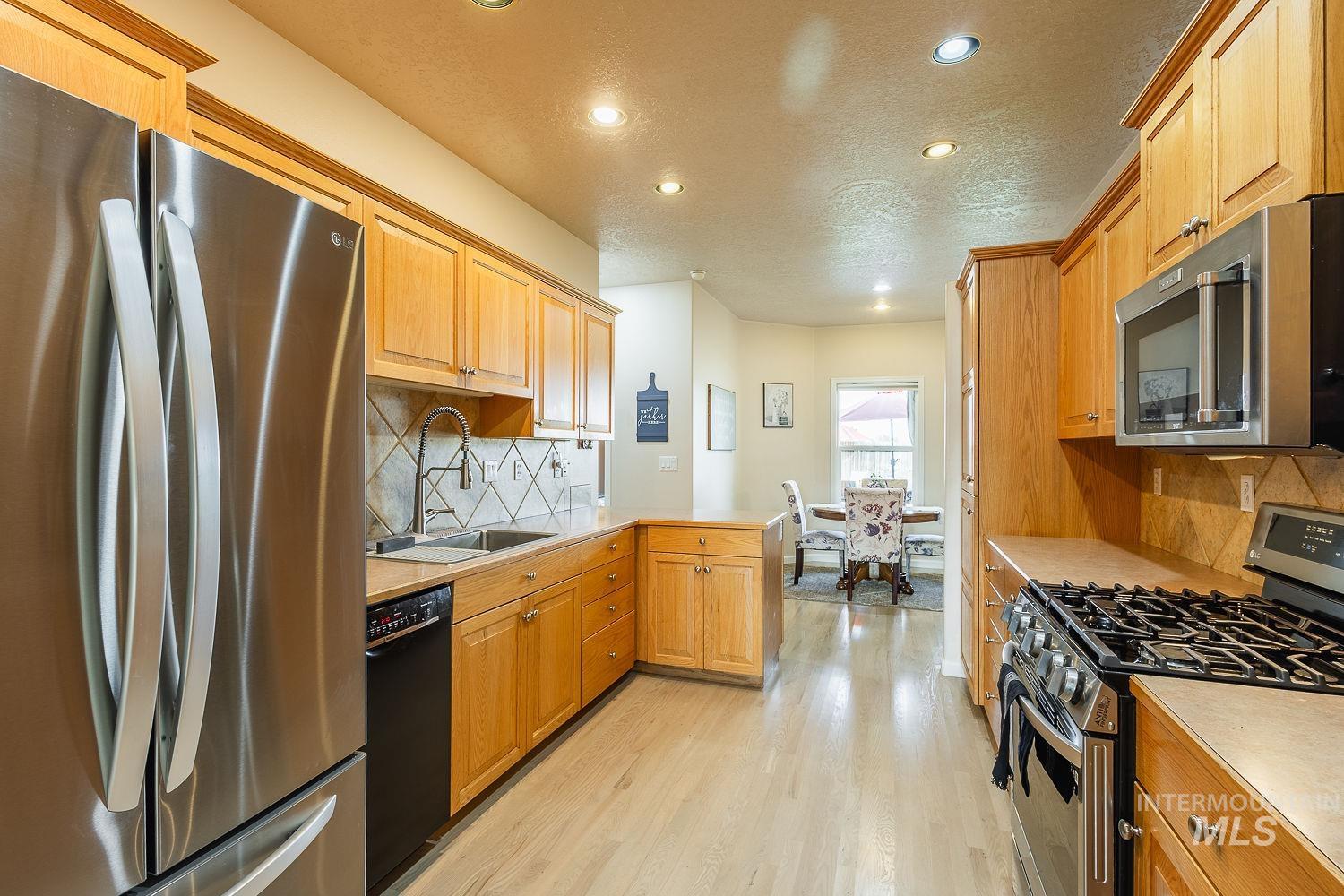 Kitchen featuring stainless steel appliances, light countertops, tasteful backsplash, light wood-style floors, and a peninsula