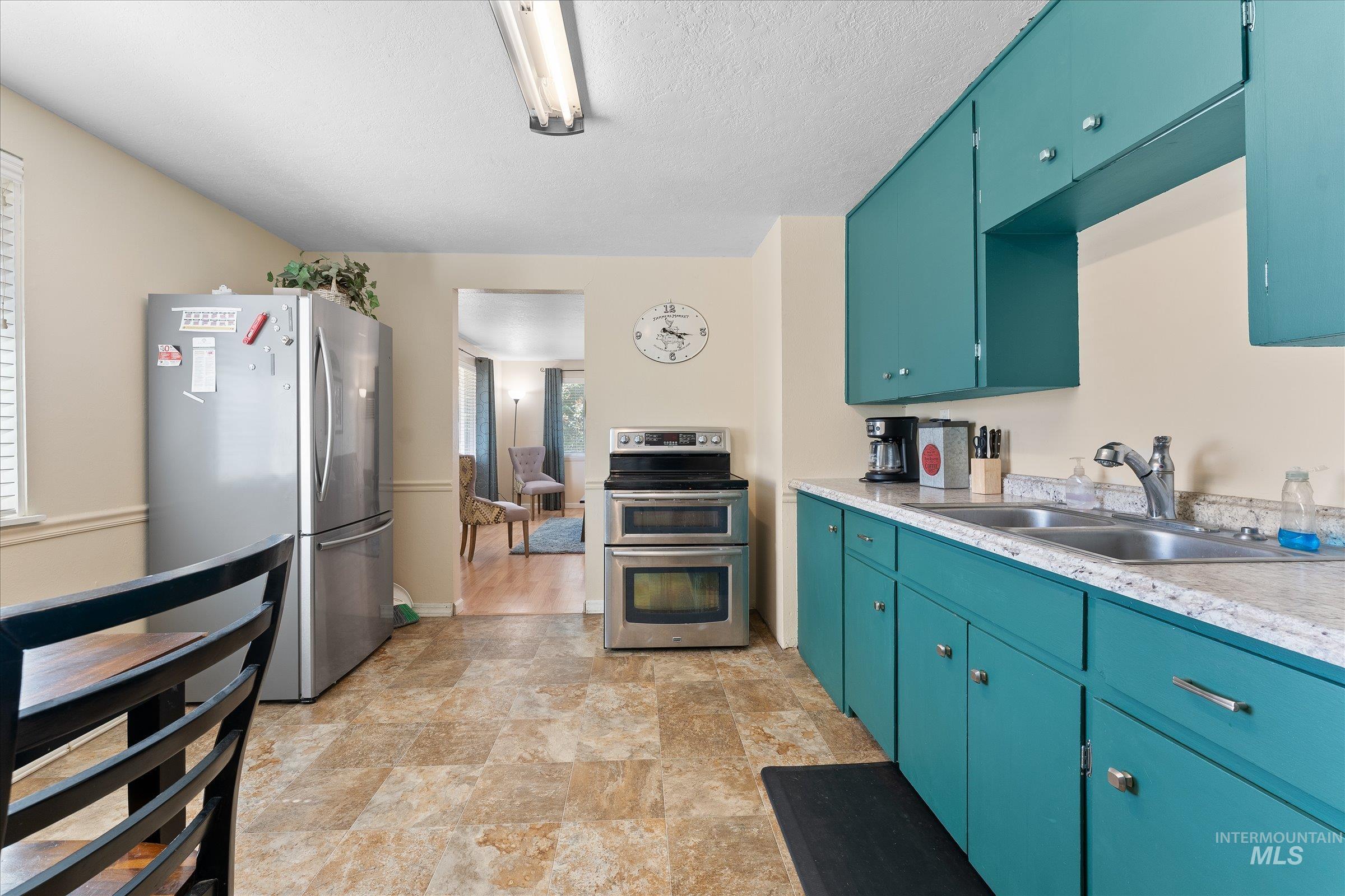 Kitchen with stainless steel appliances, light countertops, blue cabinets, stone finish flooring, and a textured ceiling