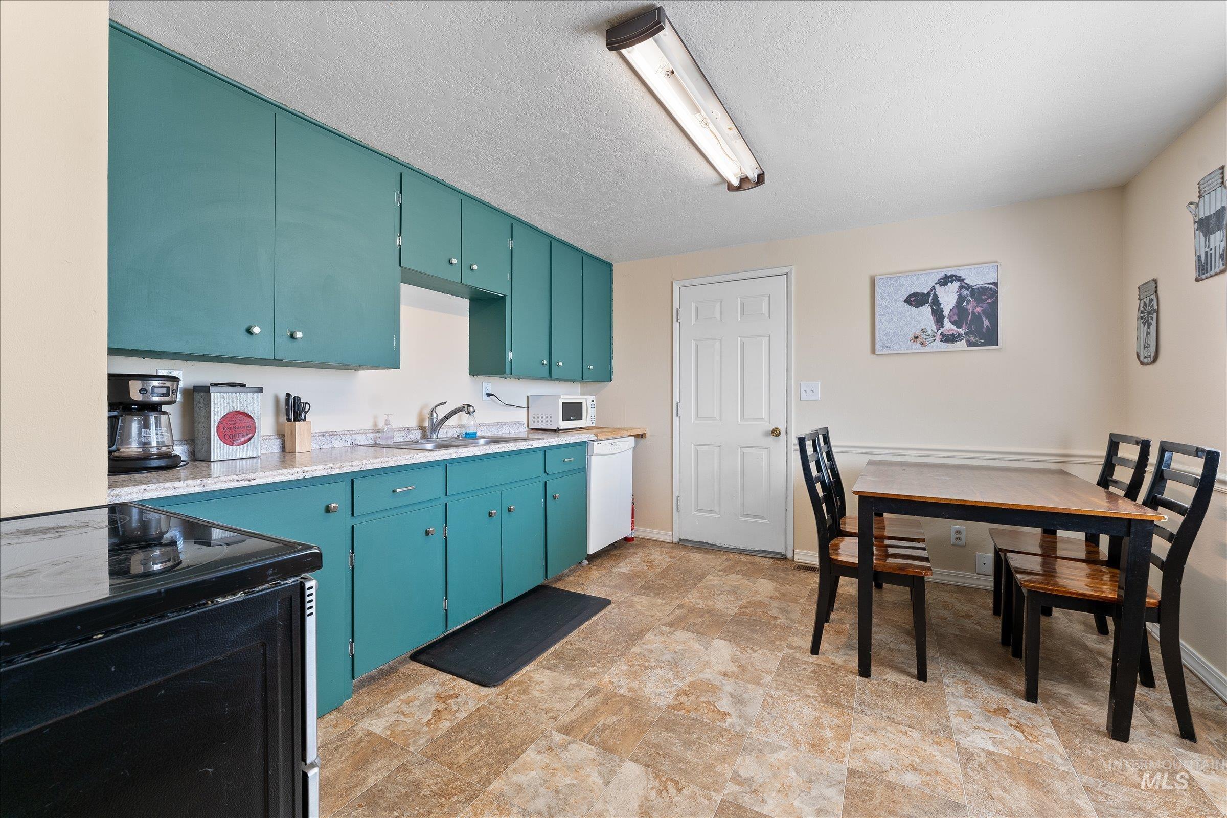 Kitchen featuring white appliances, light countertops, a textured ceiling, blue cabinets, and stone finish flooring