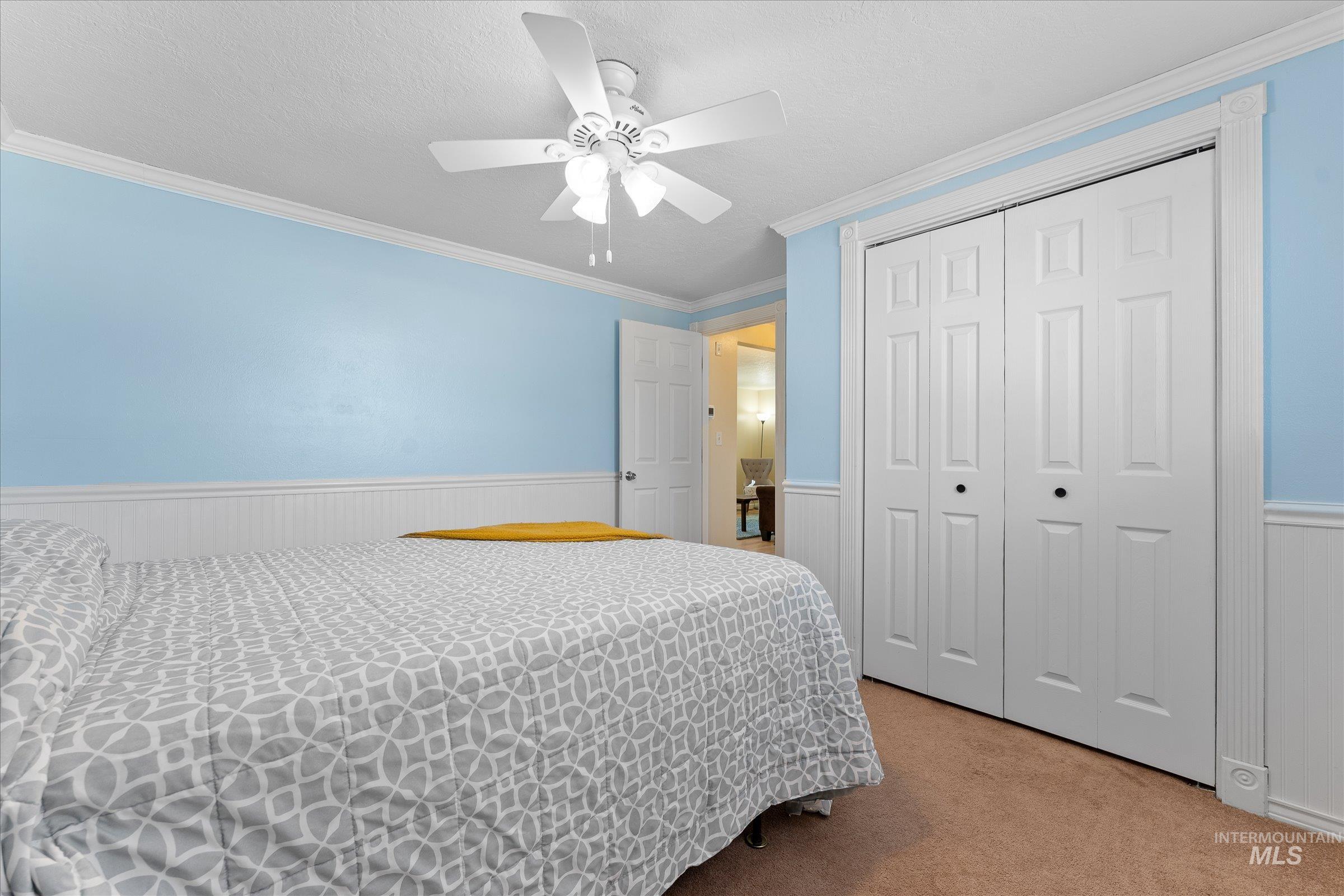 Bedroom featuring ornamental molding, a wainscoted wall, a closet, carpet, and ceiling fan