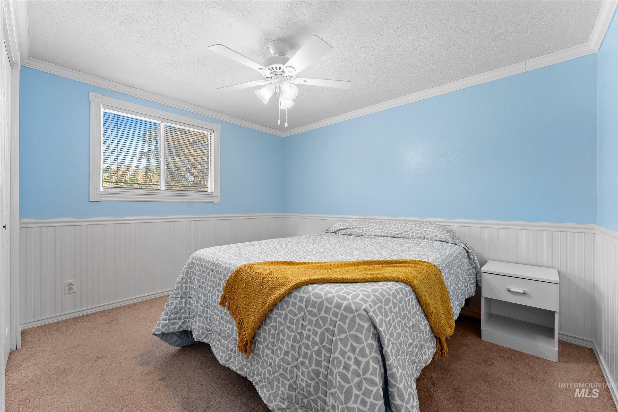 Carpeted bedroom with wainscoting, ornamental molding, and ceiling fan