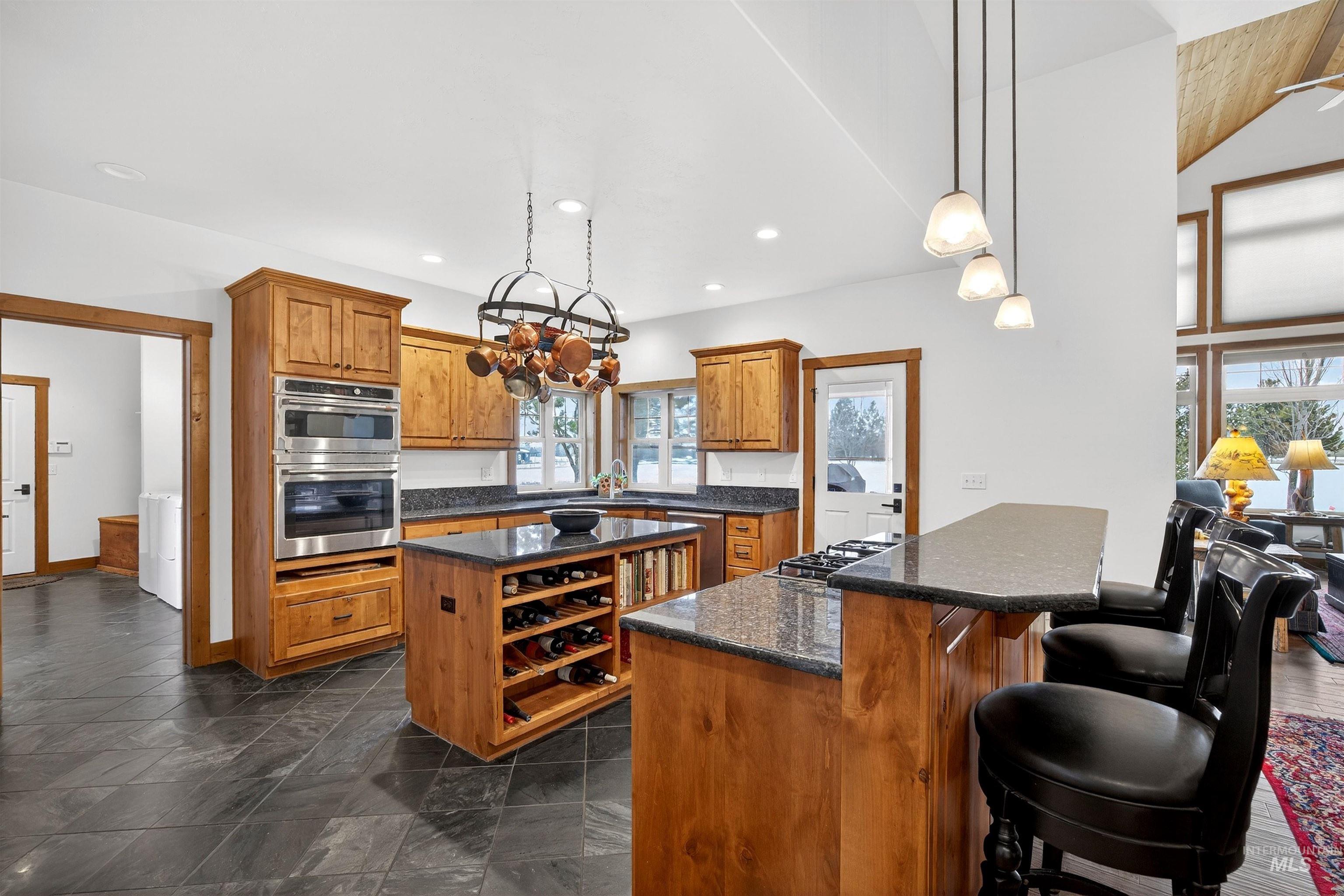 Kitchen featuring dark stone tile flooring, natural wood cabinetry, a central island with built-in wine storage, built-in stainless steel appliances, and dark countertops