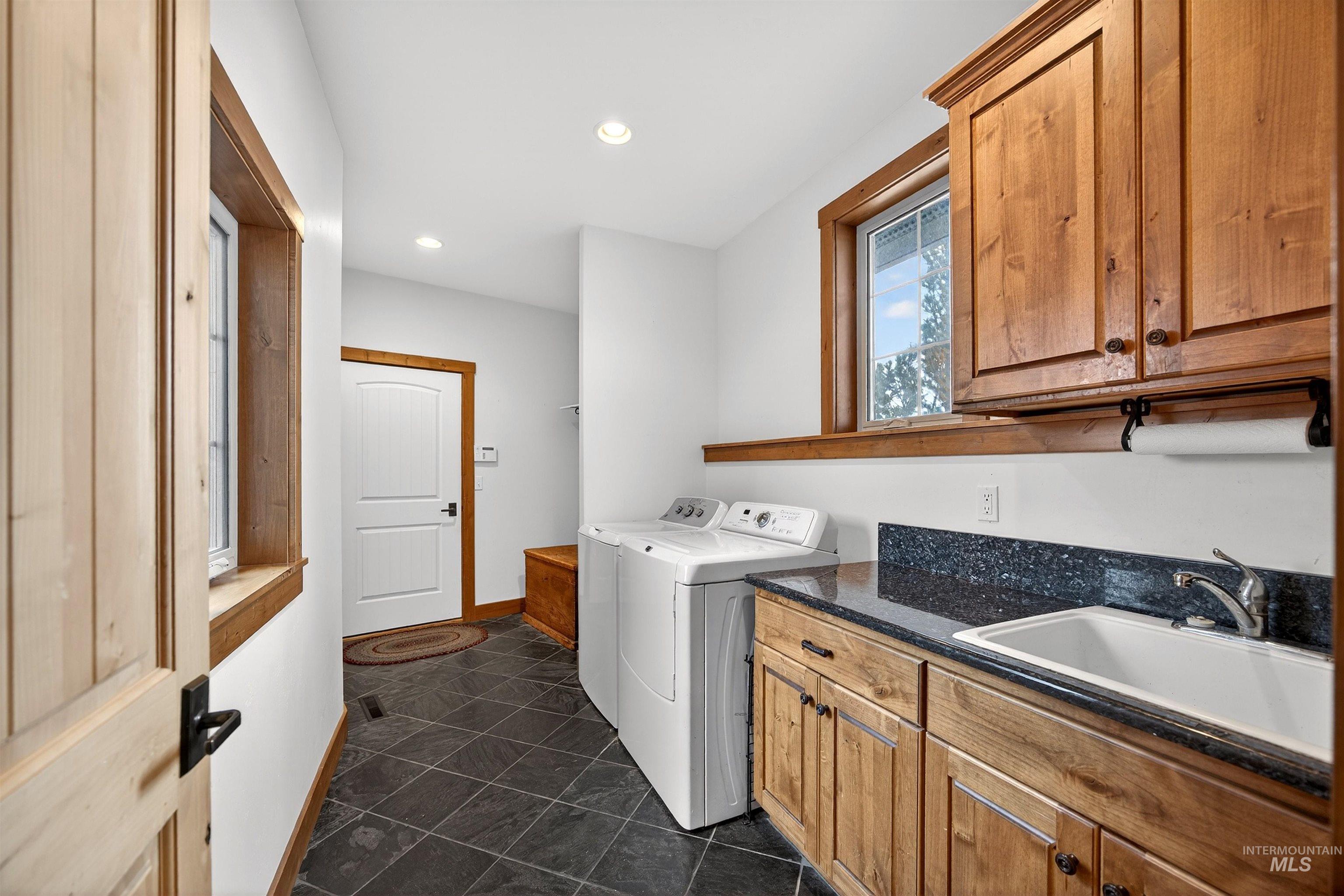 Utility room featuring slate-finish floor tile, wood-finish cabinetry, a utility sink with a chrome faucet, and a dark speckled countertop