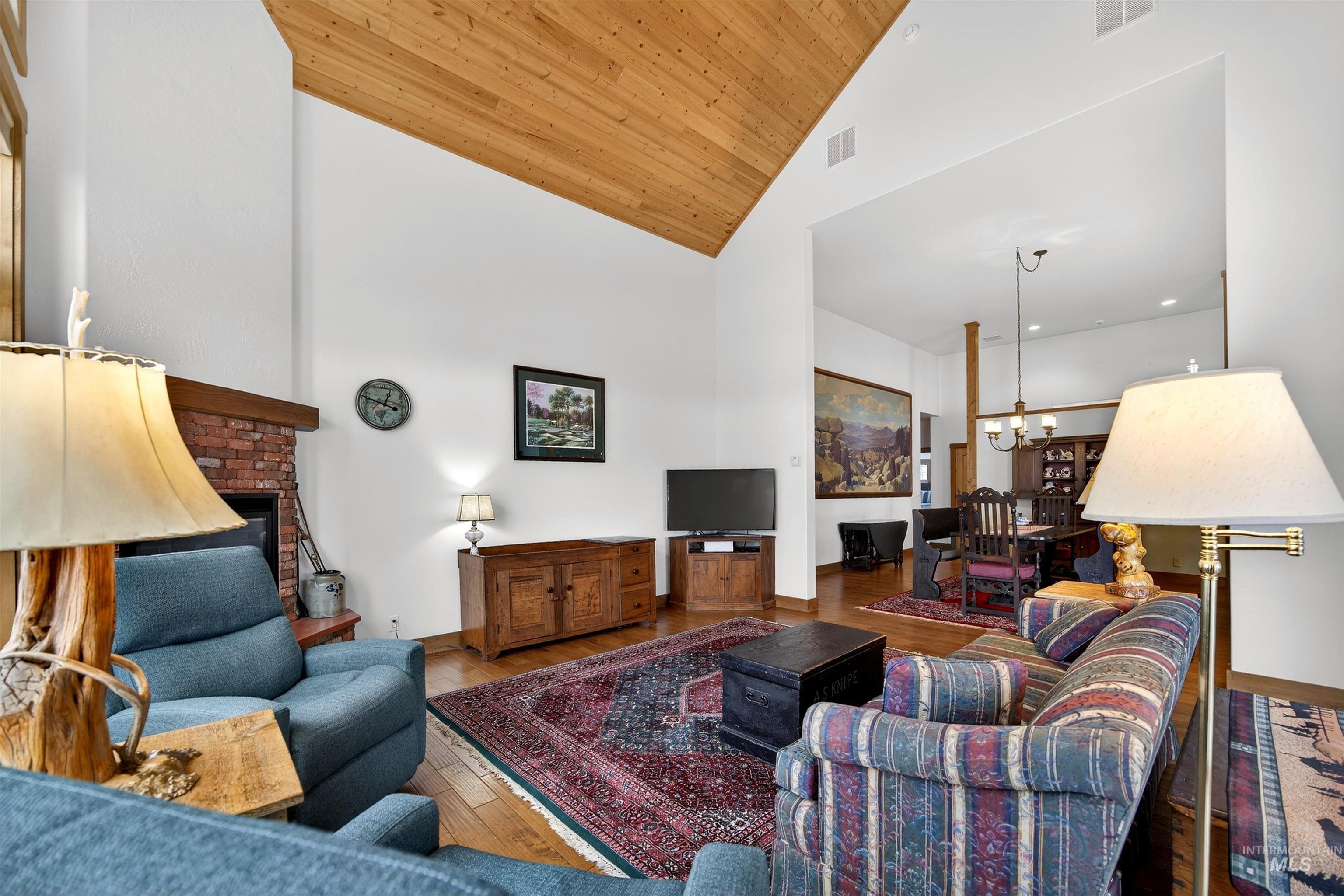 Living area with a brick fireplace, wood finished floors, a vaulted wood ceiling, and a chandelier