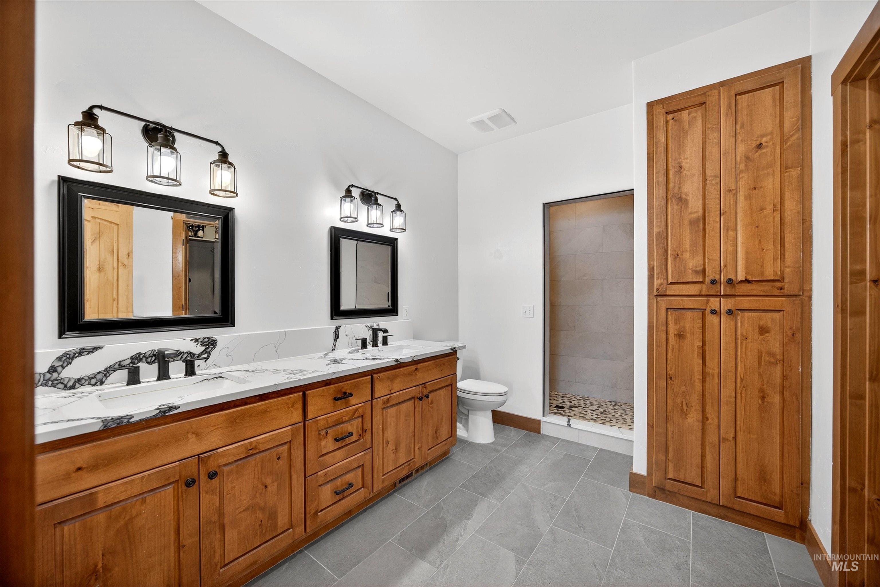 Full bath featuring double vanity, tiled shower, and light tile patterned floors