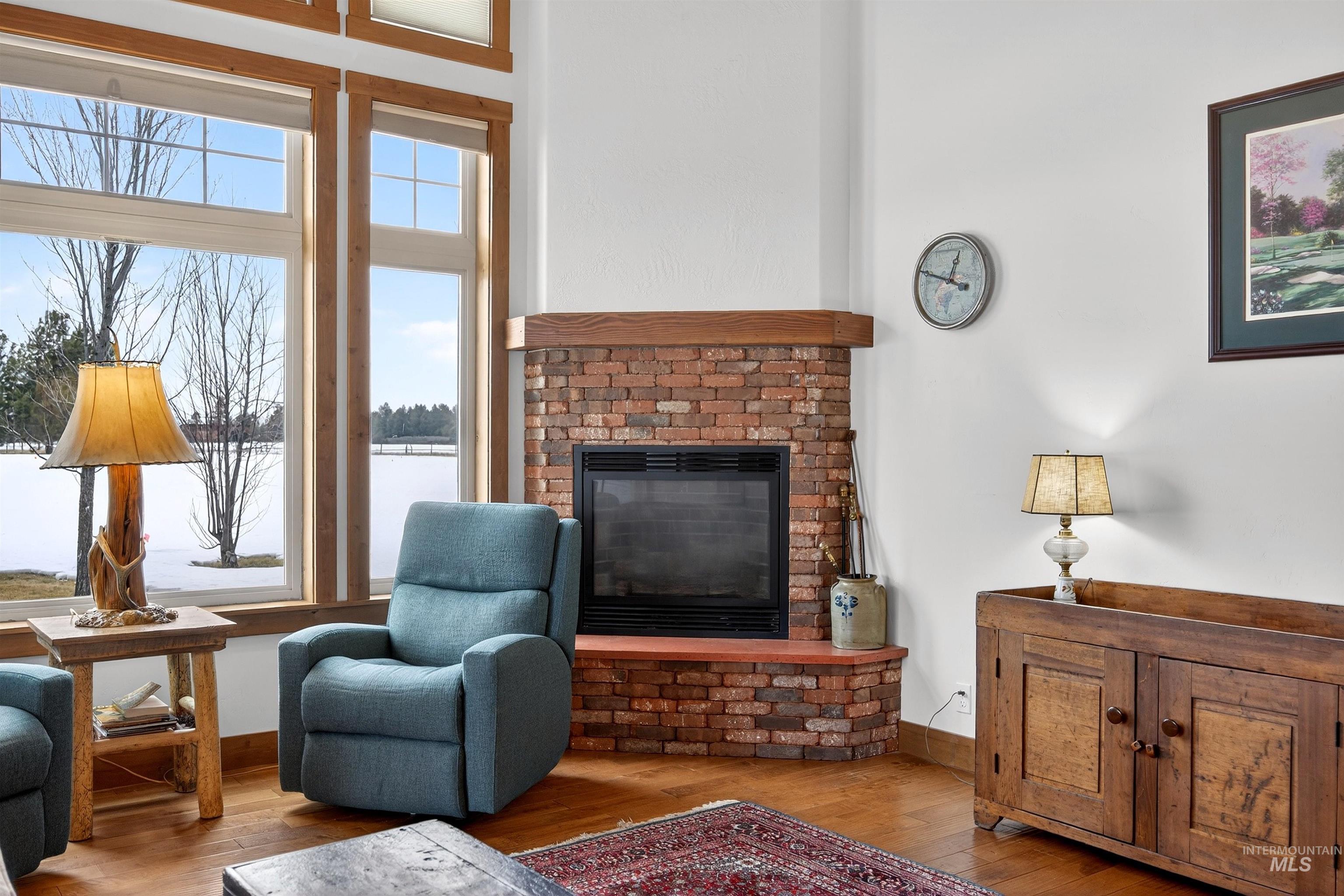 Corner brick fireplace with a wood mantel, complemented by expansive windows with wood-finish trim and wood-finish flooring