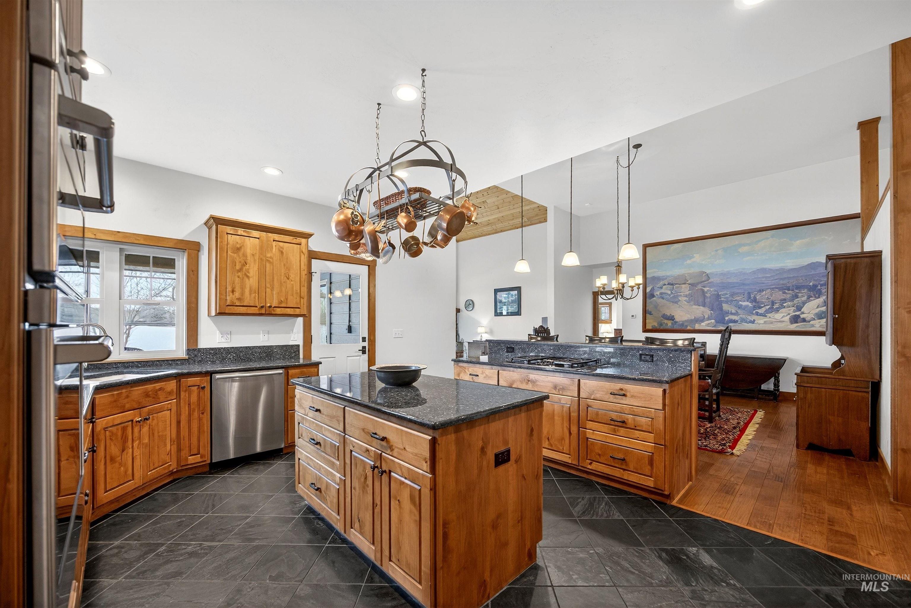 Kitchen with suspended lighting, wood finish cabinetry, stainless steel appliances, and dark stone counters