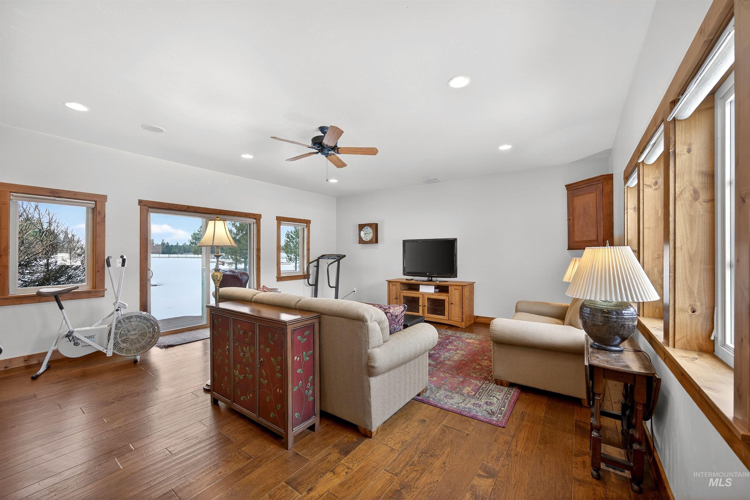 Spacious room featuring wood-finish flooring, a ceiling fan, recessed lighting, and multiple windows with wood trim