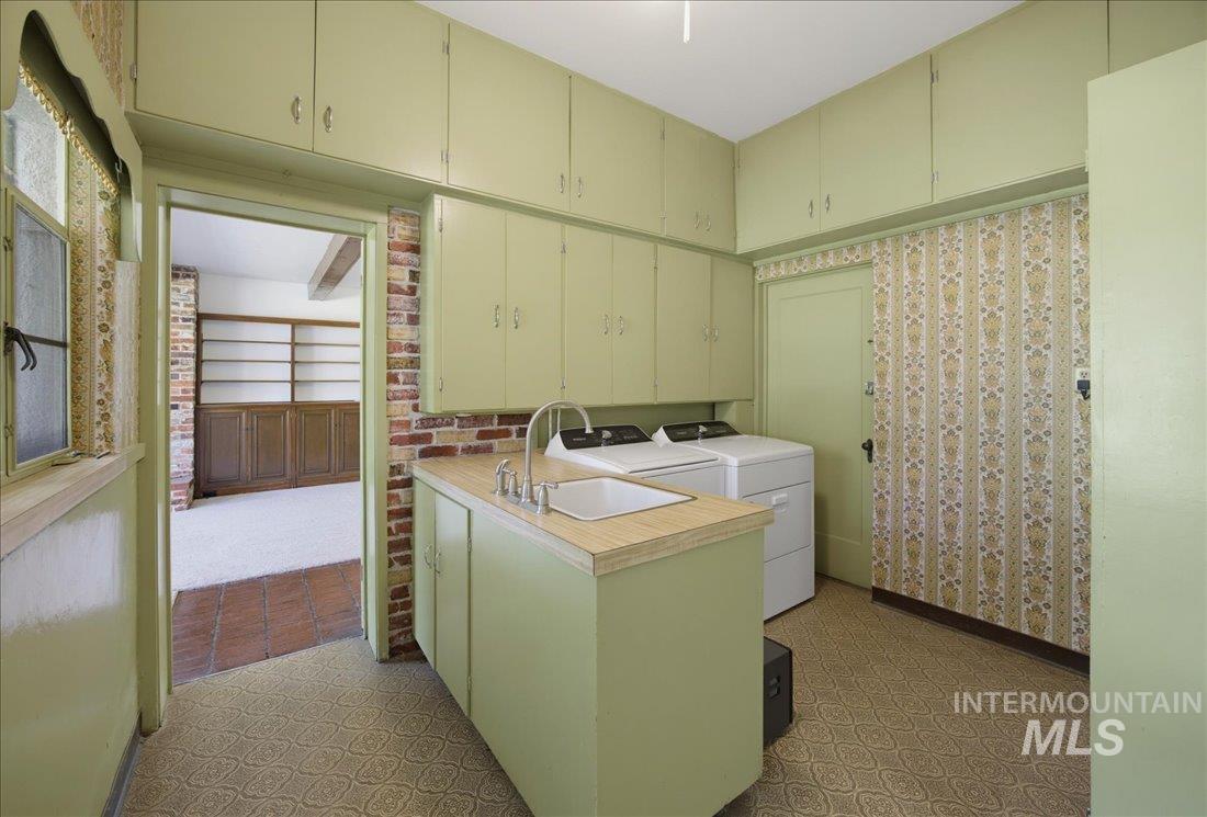 Utility room featuring extensive cabinetry, a built-in sink with countertop, patterned flooring, and brick accent wall