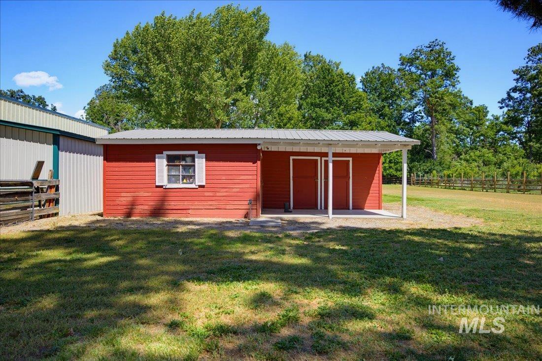 Red outbuilding with a metal roof, featuring a covered porch with white support posts and two red doors