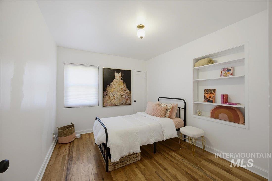 Room featuring built-in shelving, wood-finish flooring, and a single window with blinds