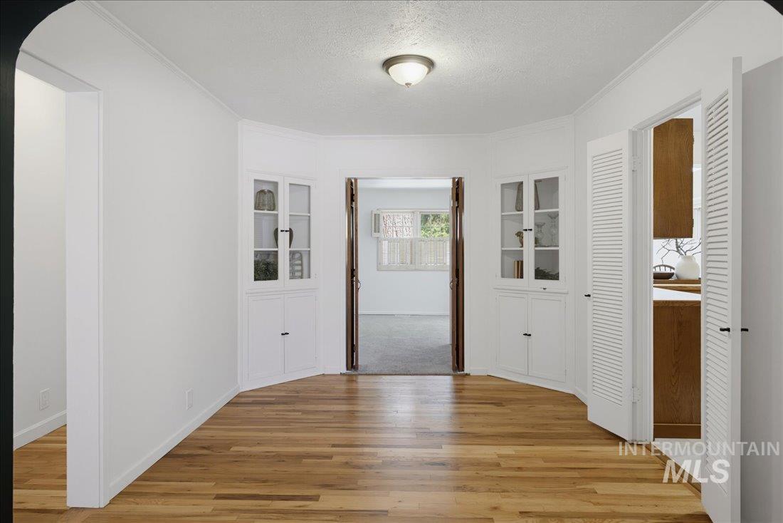 Hardwood flooring throughout the main area featuring two built-in corner display cabinets with glass doors, a ceiling-mounted light fixture, and two louvered doors