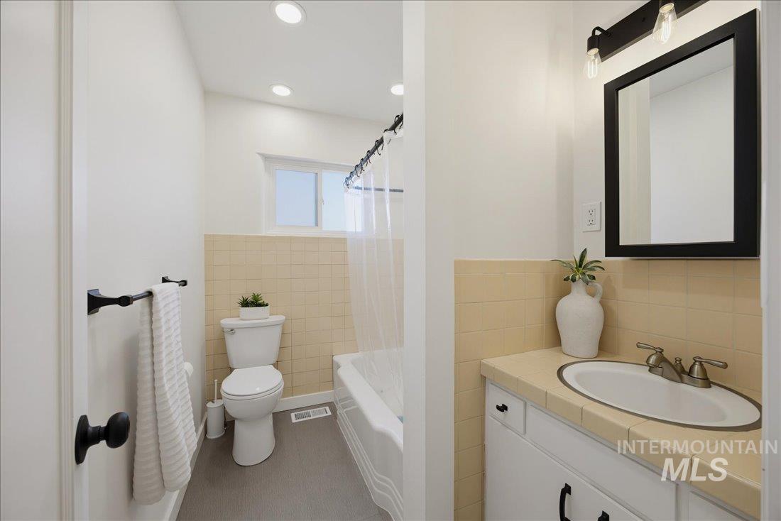 Bathroom featuring a white vanity with an integrated sink, tiled countertop, and black framed mirror