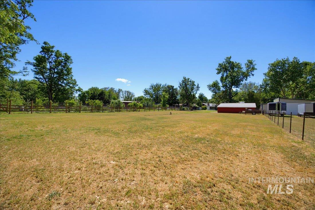Expansive outdoor space featuring a large grassy area, wood-post fencing, and a red barn structure