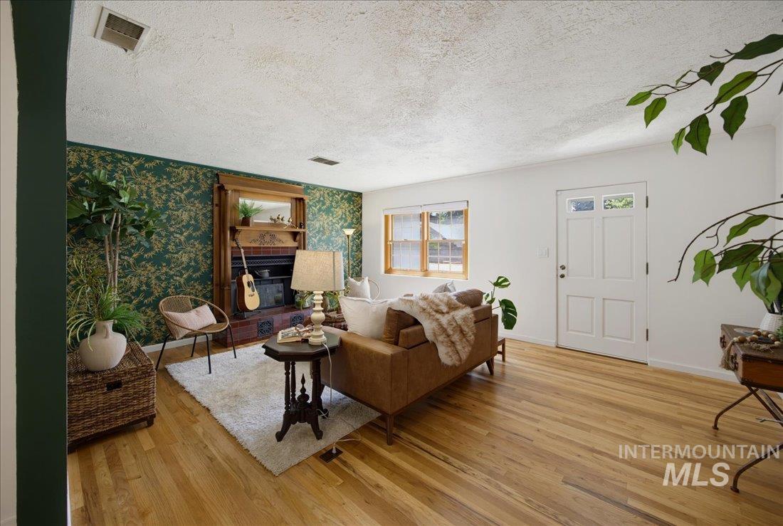 Hardwood flooring throughout the main living area, featuring a decorative fireplace with an ornate wood mantel, an accent wall with botanical-patterned wallpaper, and a multi-pane front door