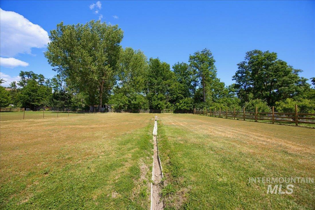 Expansive outdoor space featuring a large grassy area, mature trees, and a wood split-rail fence