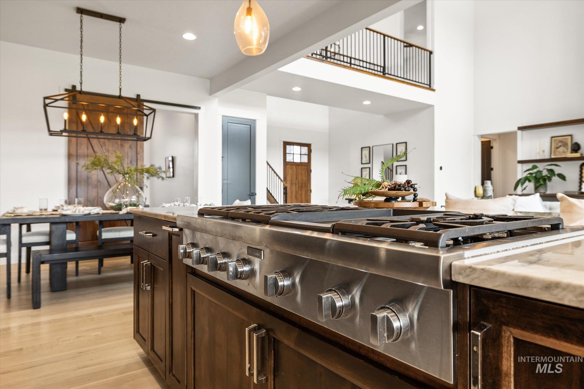 Kitchen with stainless steel gas stovetop, dark brown cabinetry, pendant lighting, light wood-type flooring, and open floor plan