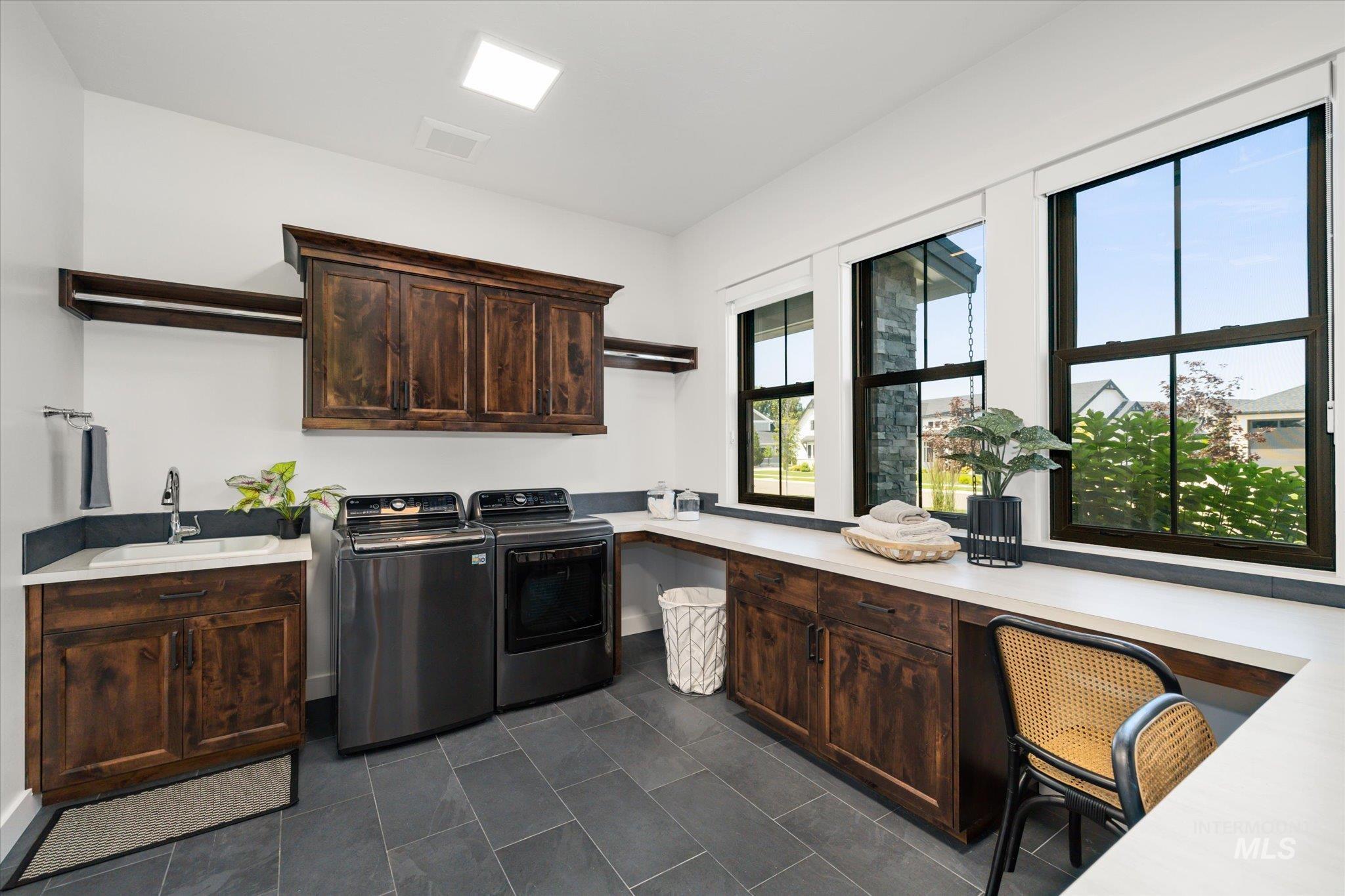 Washroom featuring washing machine and dryer, cabinet space, a desk, and dark tile patterned flooring