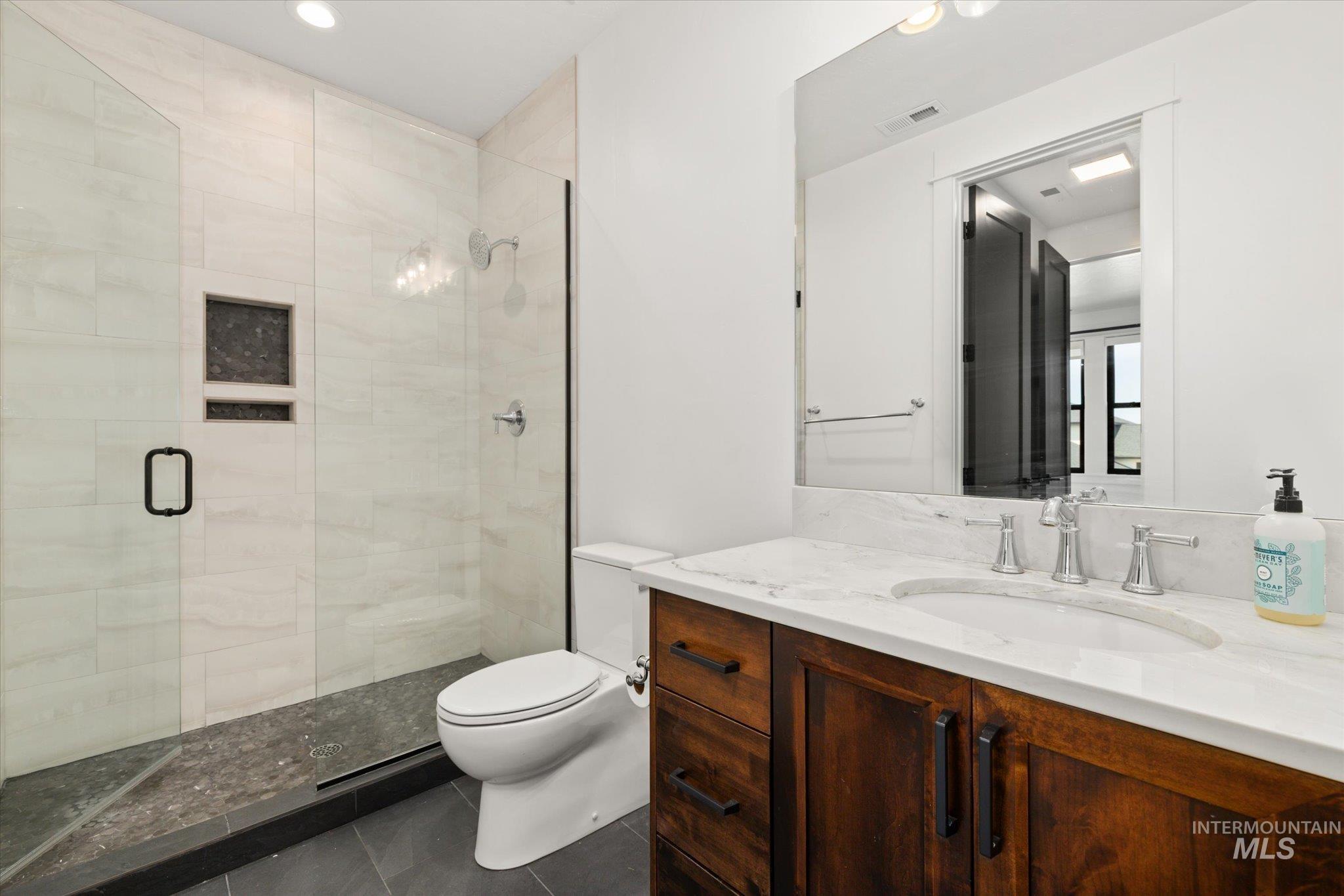 Bathroom featuring vanity, a shower stall, tile patterned flooring, and recessed lighting
