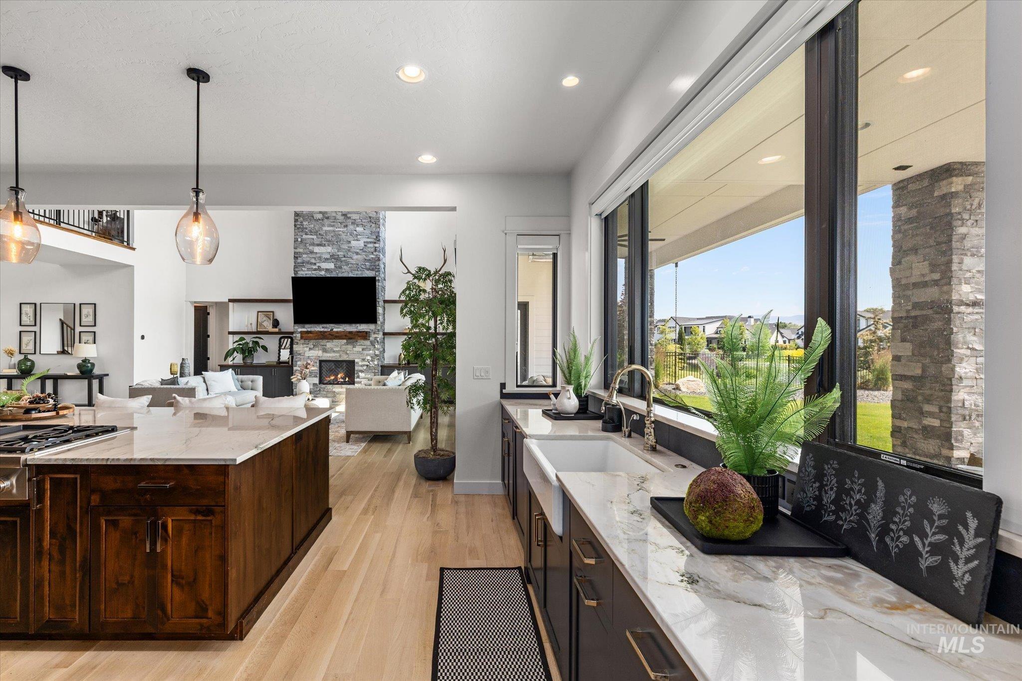 Kitchen featuring light wood-style floors, a stone fireplace, light stone counters, dark brown cabinetry, and decorative light fixtures