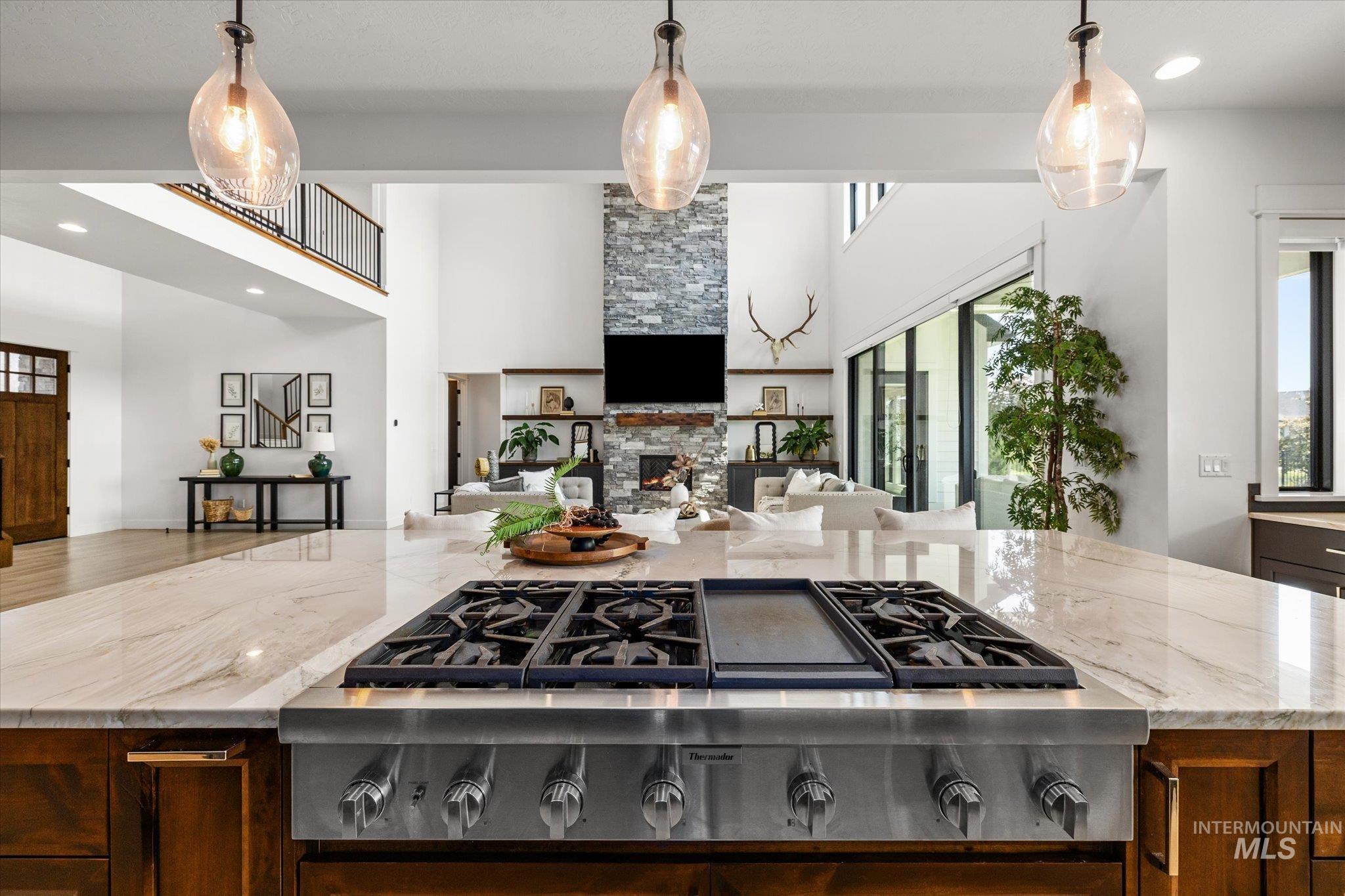 Kitchen featuring open floor plan, stainless steel gas cooktop, a stone fireplace, a towering ceiling, and light stone counters