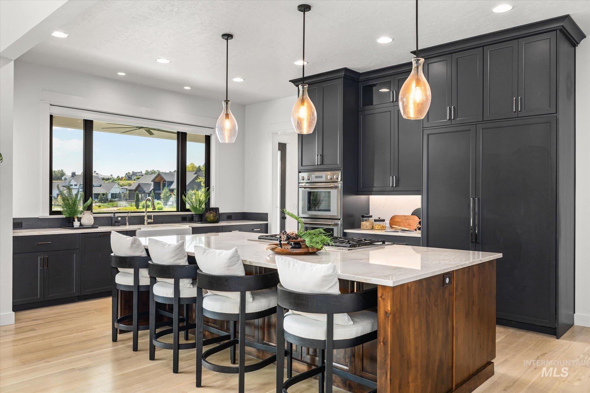 Kitchen featuring light stone counters, light wood-style floors, appliances with stainless steel finishes, a center island with sink, and recessed lighting