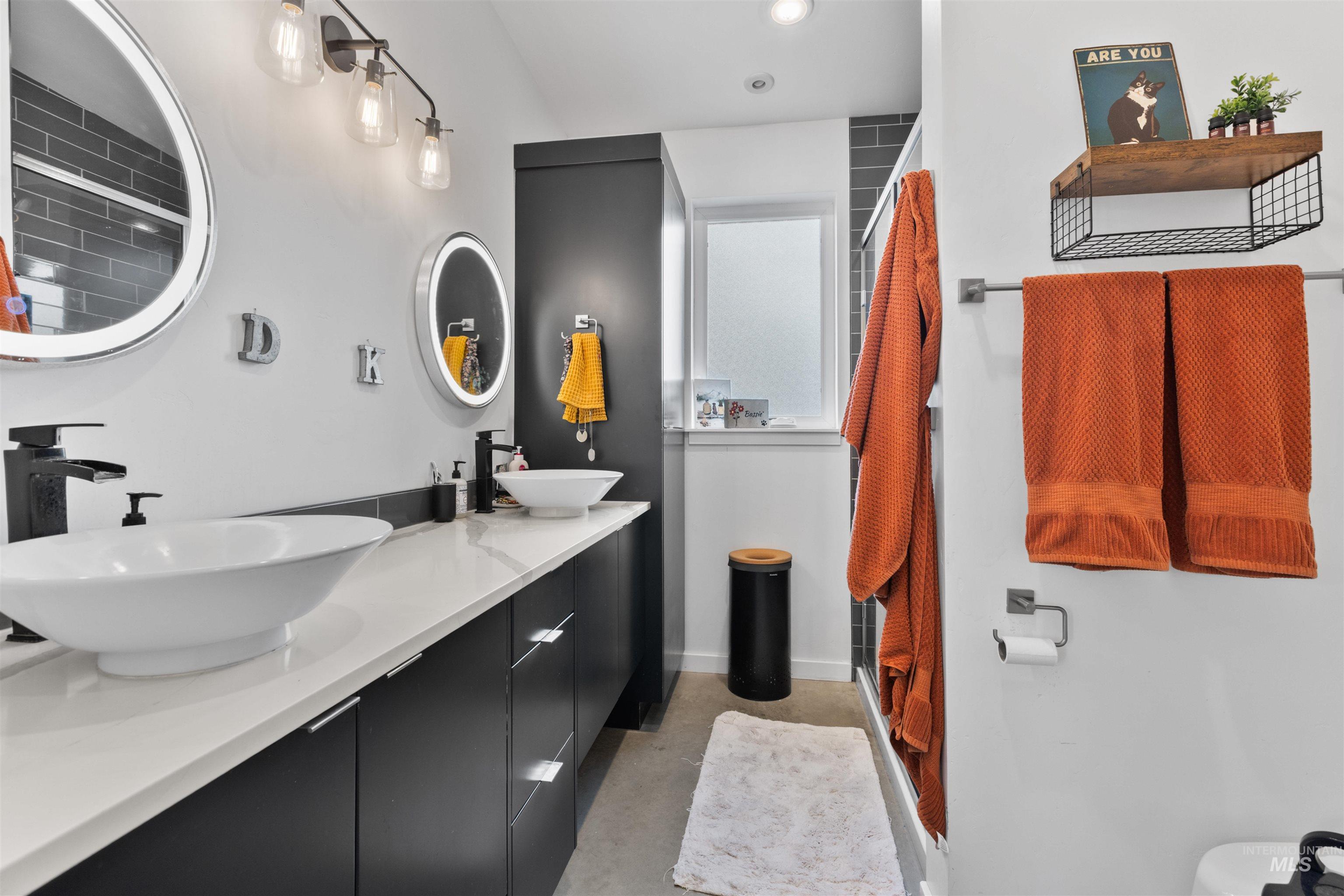 Full bathroom featuring double vanity, a shower with shower door, and finished concrete flooring