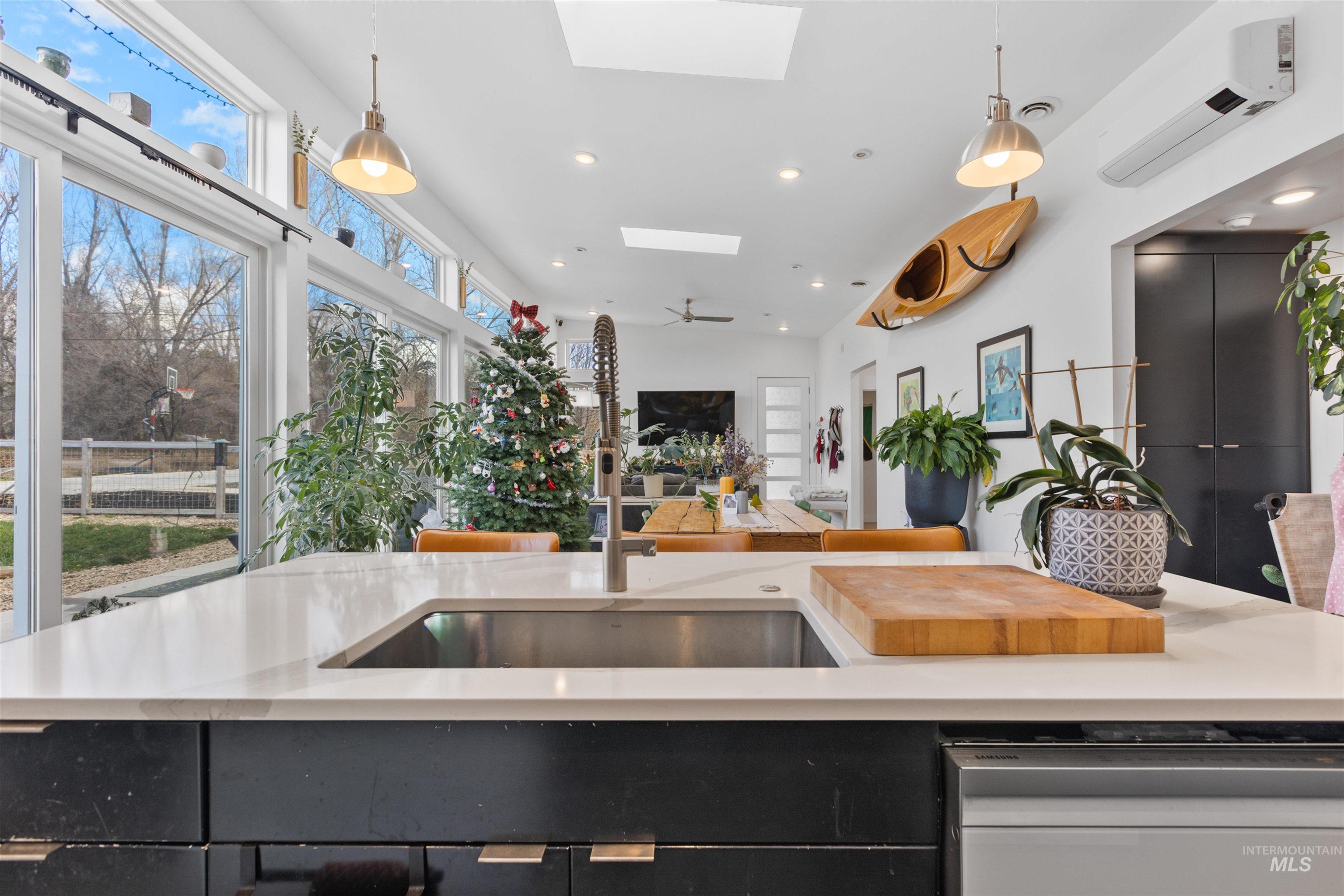 Kitchen featuring dark cabinetry, a skylight, hanging light fixtures, stainless steel dishwasher, and open floor plan