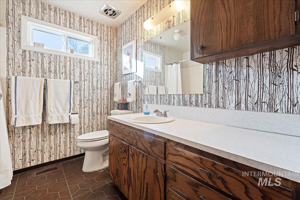 Bathroom with curtained shower, vanity, dark tile patterned flooring, and wallpapered walls