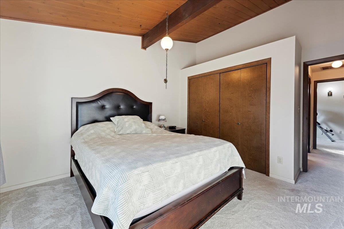 Bedroom featuring light colored carpet, a wood ceiling with exposed beams, and a closet