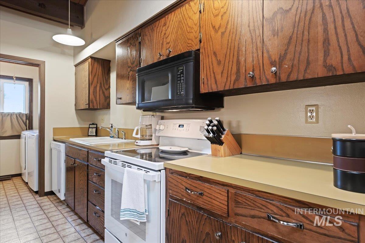 Kitchen featuring white appliances, light countertops, pendant lighting, and washer / clothes dryer