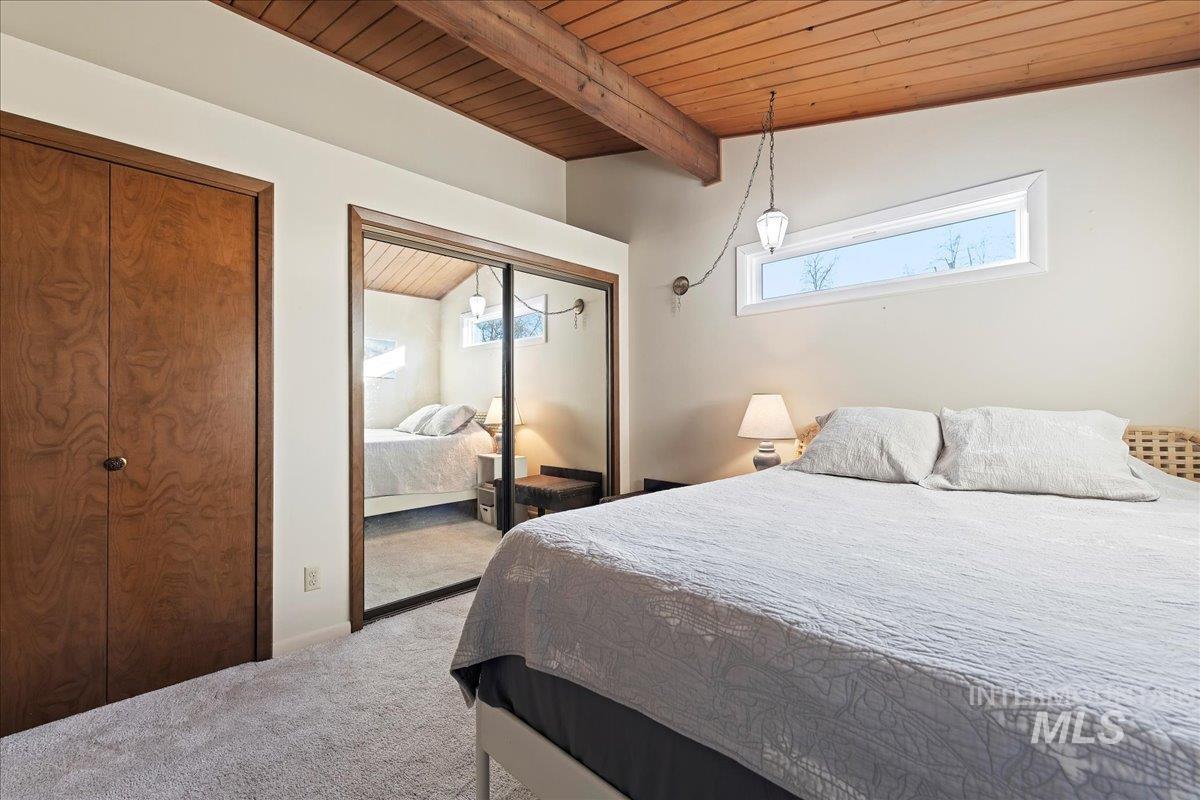 Carpeted bedroom featuring a wood ceiling with exposed beams and multiple closets
